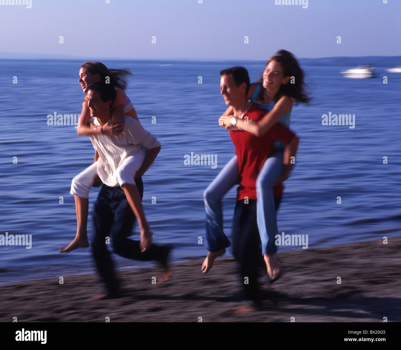 Youngsters teenagers Two pairs couples lake fun joke Piggyback race running action Dynamic summer holida Stock Photo