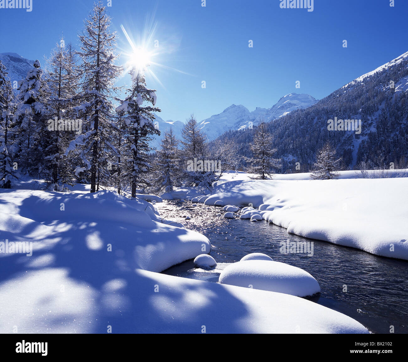 scenery landscape winter brook stream wood coniferous forest snow mountains Alps sun winter scenery Bernin Stock Photo