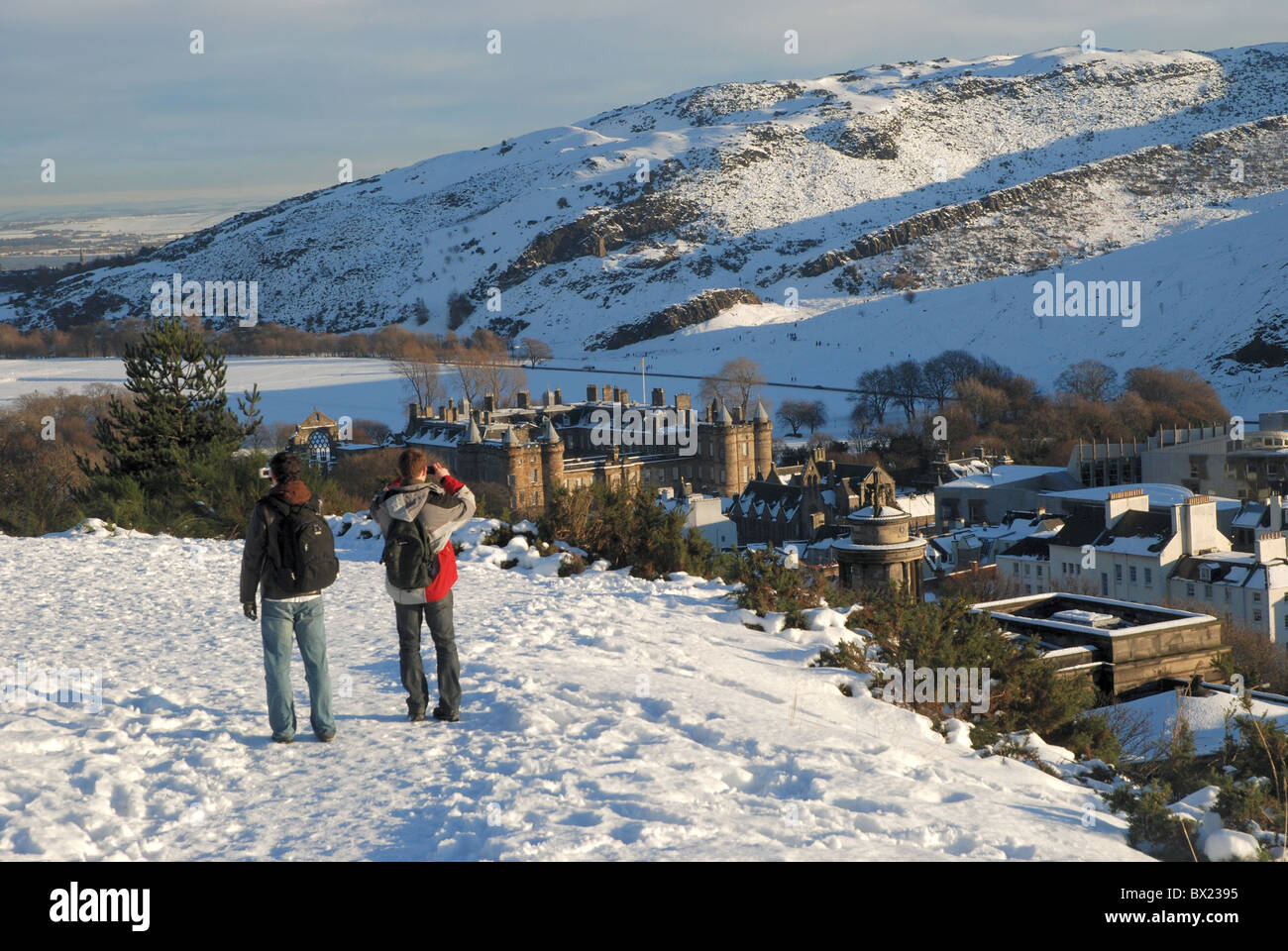 Two tourists walking on a snowy Calton Hill in Edinburgh and photographing the view toward Holyrood Palace. Stock Photo