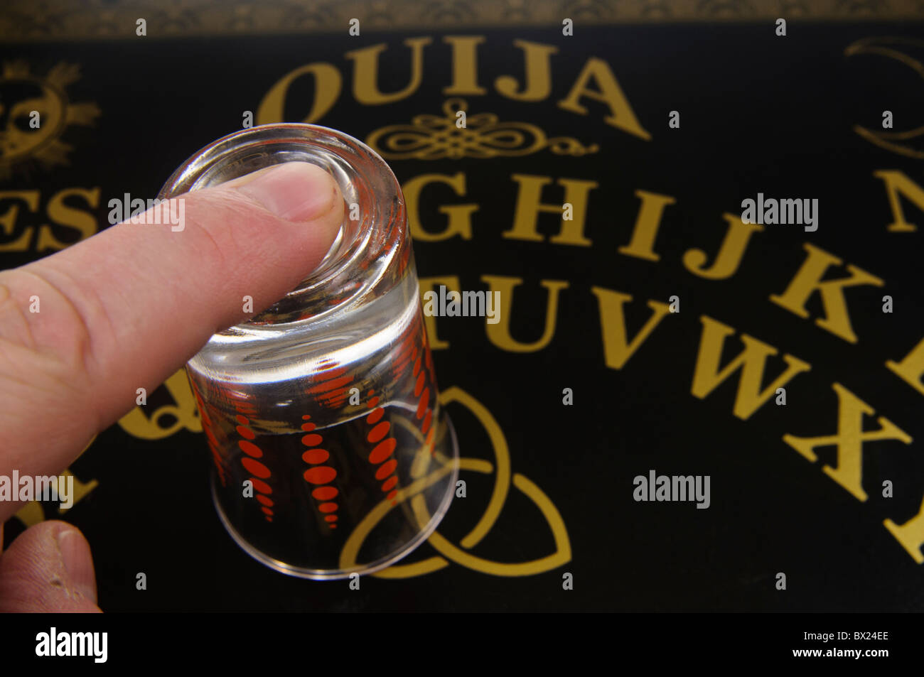 Finger on top of a glass on a generic Ouija board Stock Photo