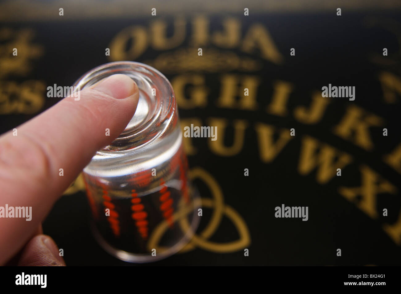 Finger on top of a glass on a Ouija board Stock Photo