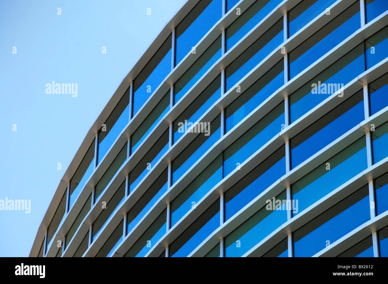 Curved exterior windows of a commercial office building reflecting a blue sky Stock Photo