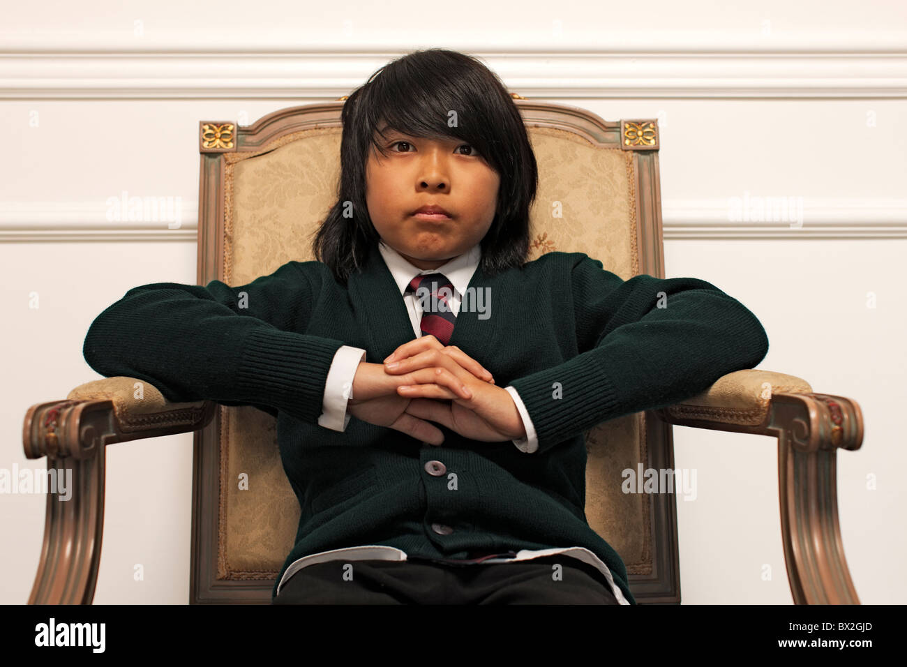 Serious Vietnamese boy sitting on elegant chair Stock Photo