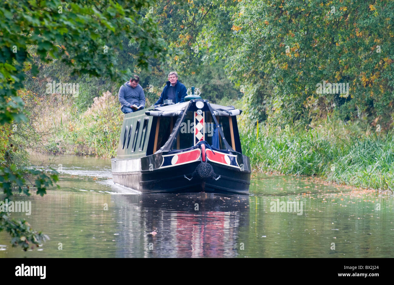 Two people navigating a river on a narrow canal boat barge heading ...