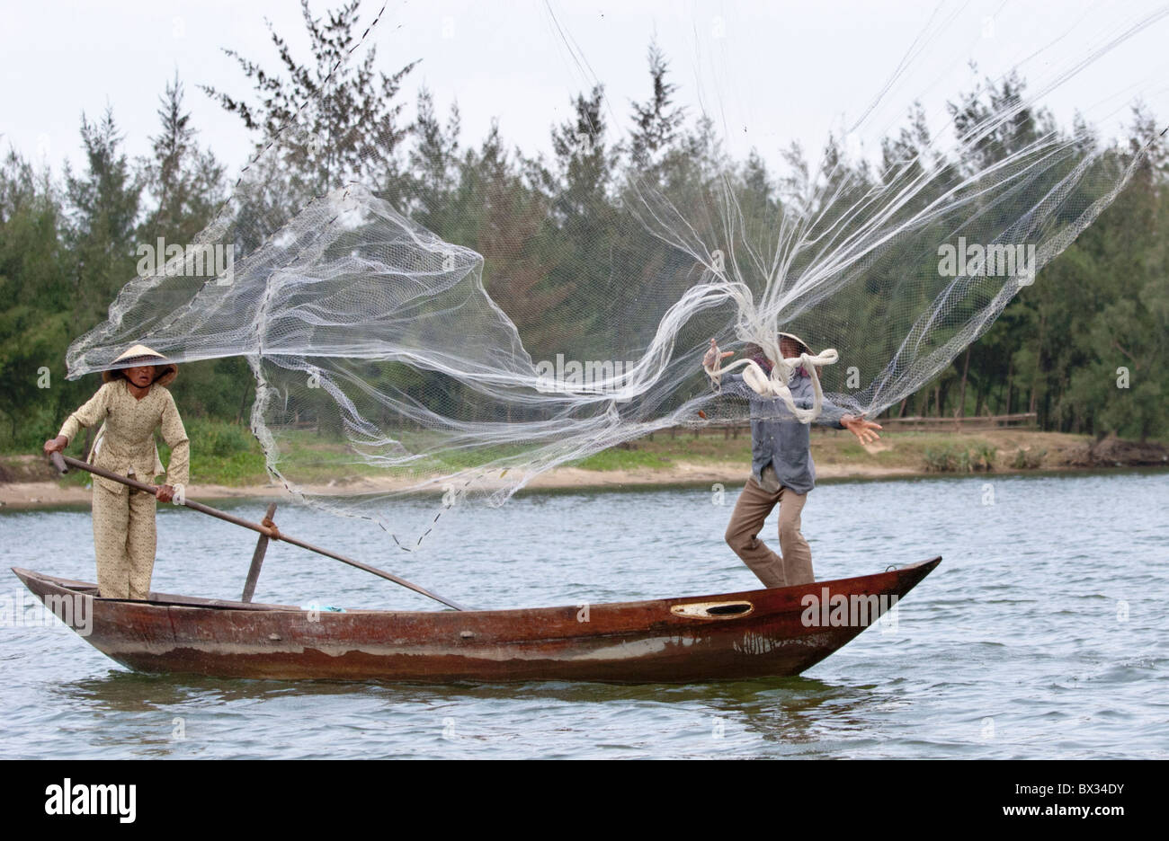 Vietnamese fisherman casting his hand-net from a small boat (rowed by his  wife) in the traditional manner Stock Photo - Alamy