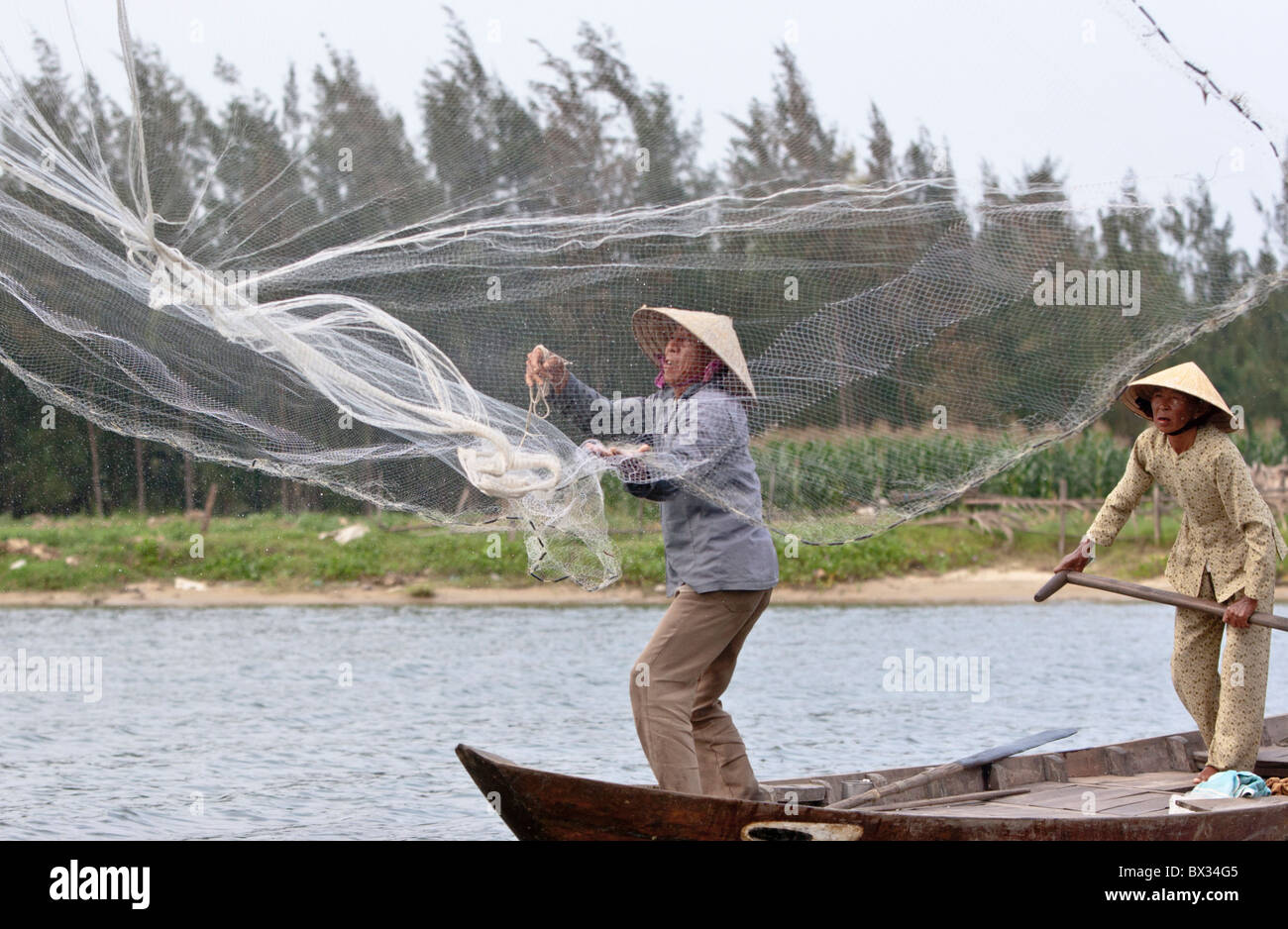 Vietnamese fisherman casting his hand-net from a small boat (rowed by ...