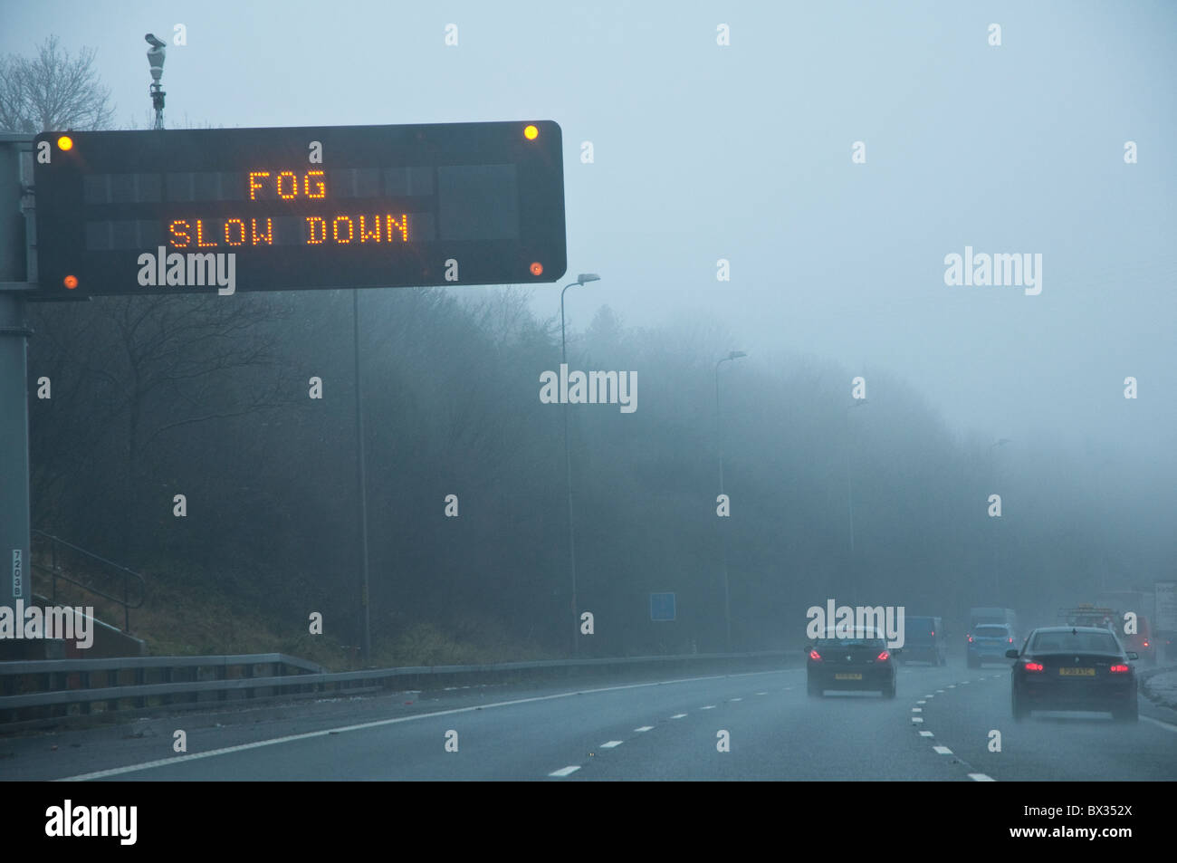 'Fog Slow Down' - motorway warning sign.  Drivers viewpoint with cars and poor visibility.  M5, UK. Stock Photo