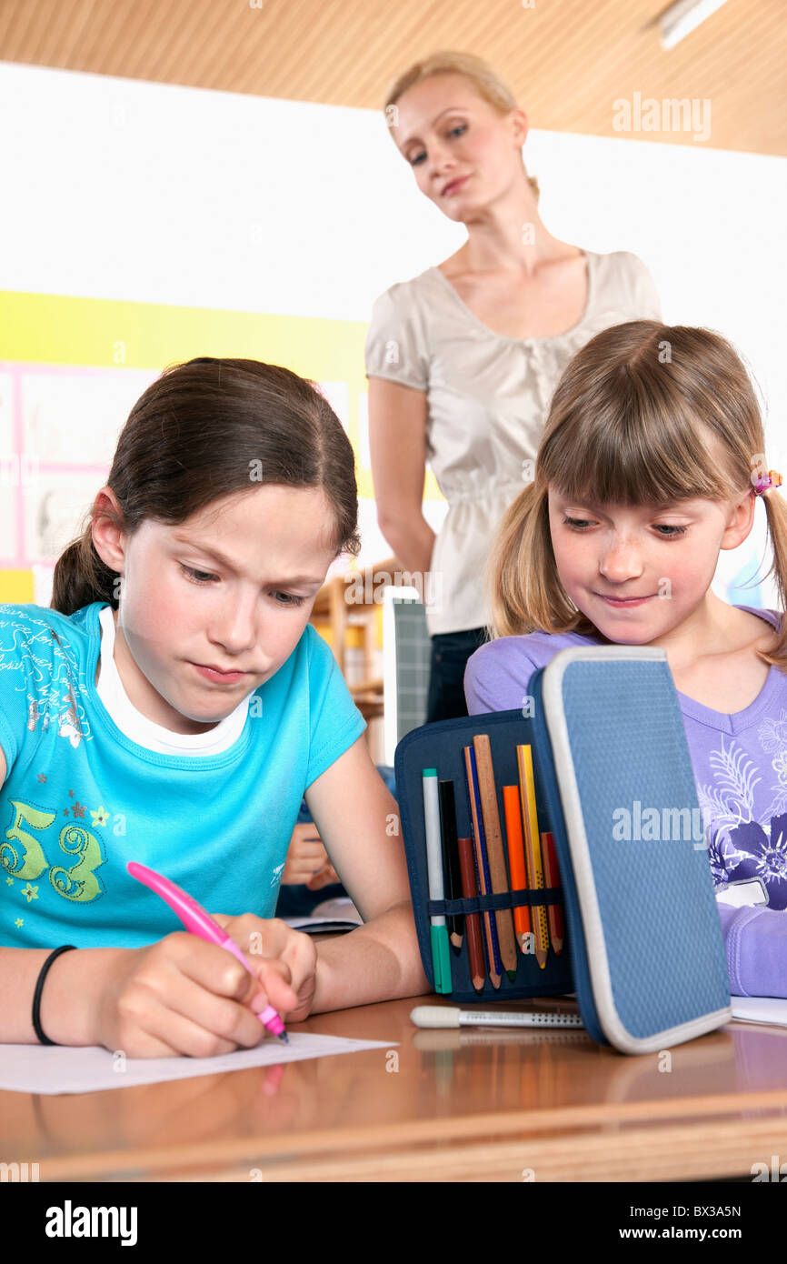 teacher watching two young girls writing test Stock Photo