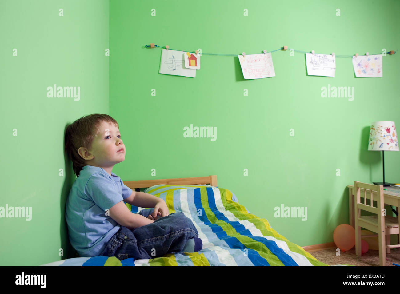 young boy sitting on bed in children´s room Stock Photo Alamy