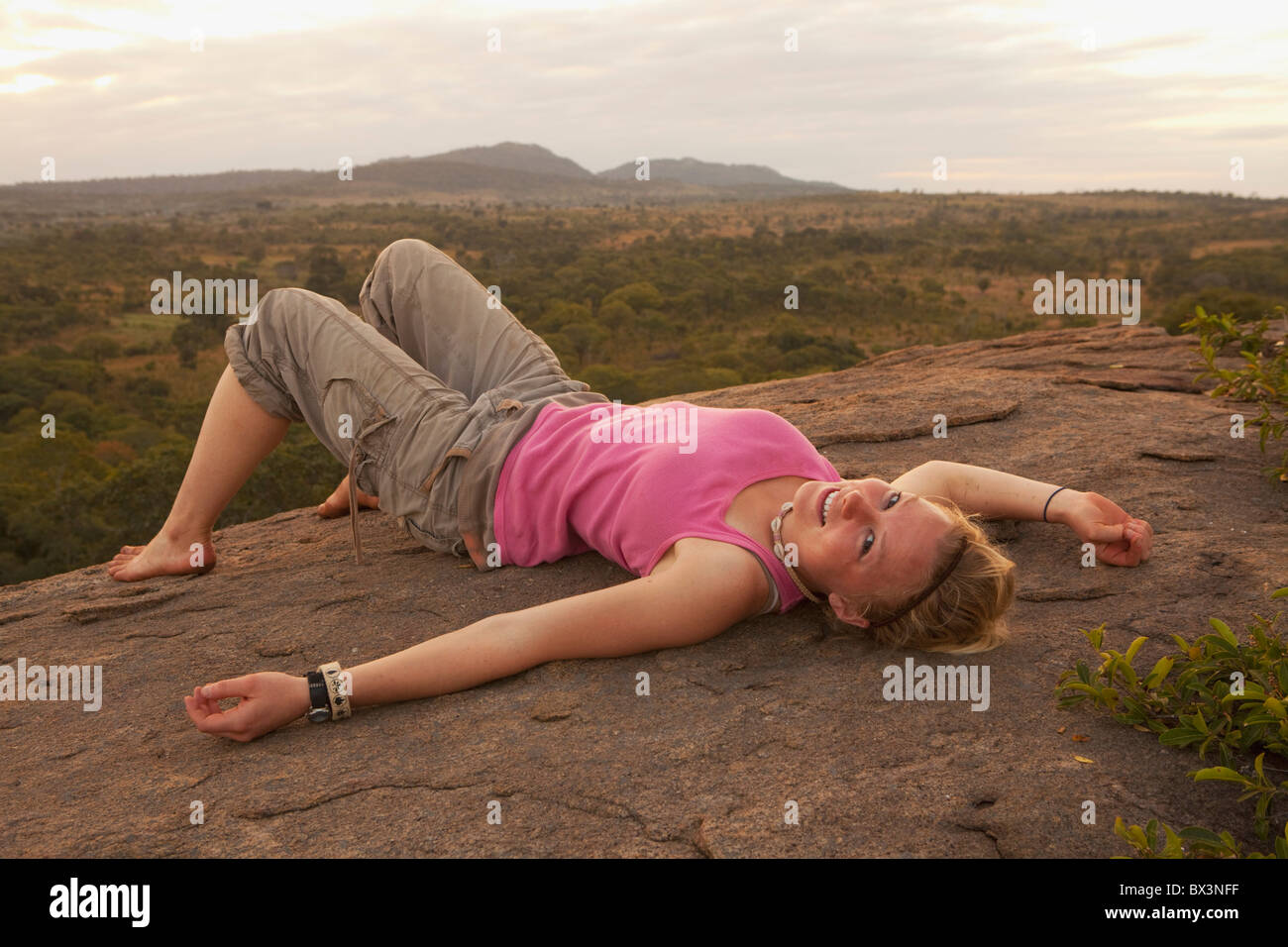 A Young Woman Lays On Her Back On A Rock With The African Landscape In The Background; Manica, Mozambique, Africa Stock Photo