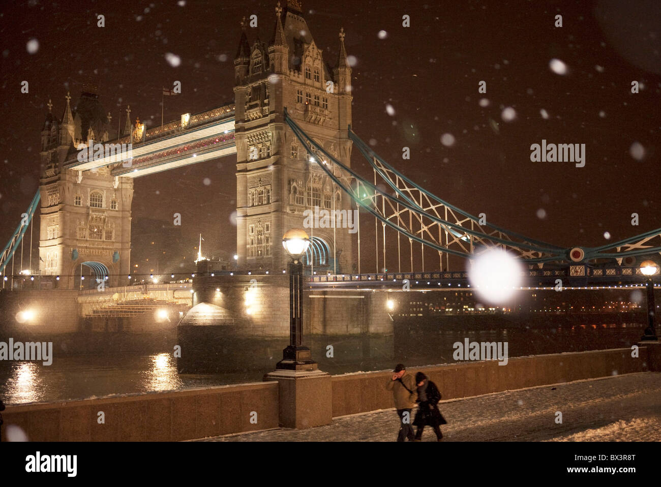 Night scene of Tower Bridge in London on a cold winter evening as snow fills the air and is blown by strong wind. Stock Photo