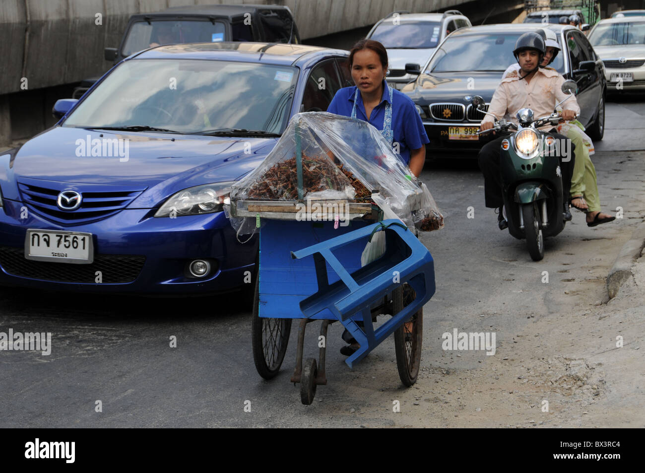 Asian pushes her cart past a traffic jam in Bangkok Stock Photo