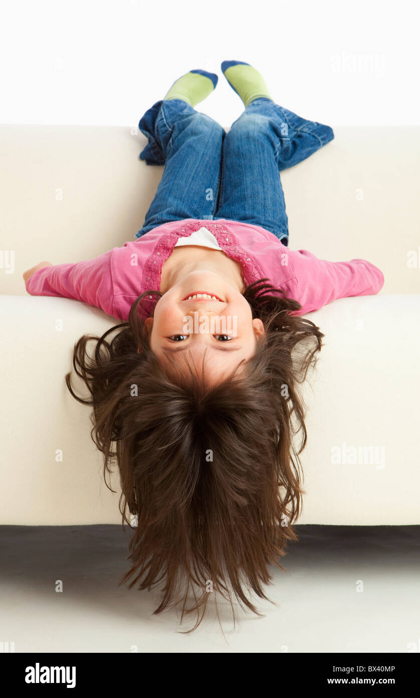 A Girl Hanging Upside Down From The Couch Stock Photo