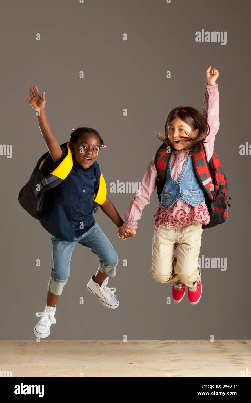 Two Girls With Backpacks Holding Hands And Jumping Into The Air Stock Photo