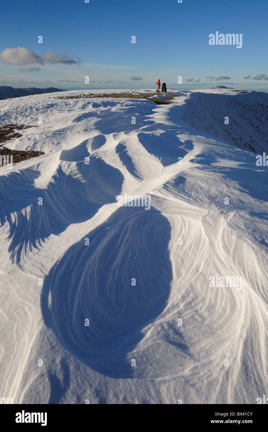 Wind blown sculpted snow patterns and walker on the summit of Helvellyn in the English Lake District Stock Photo