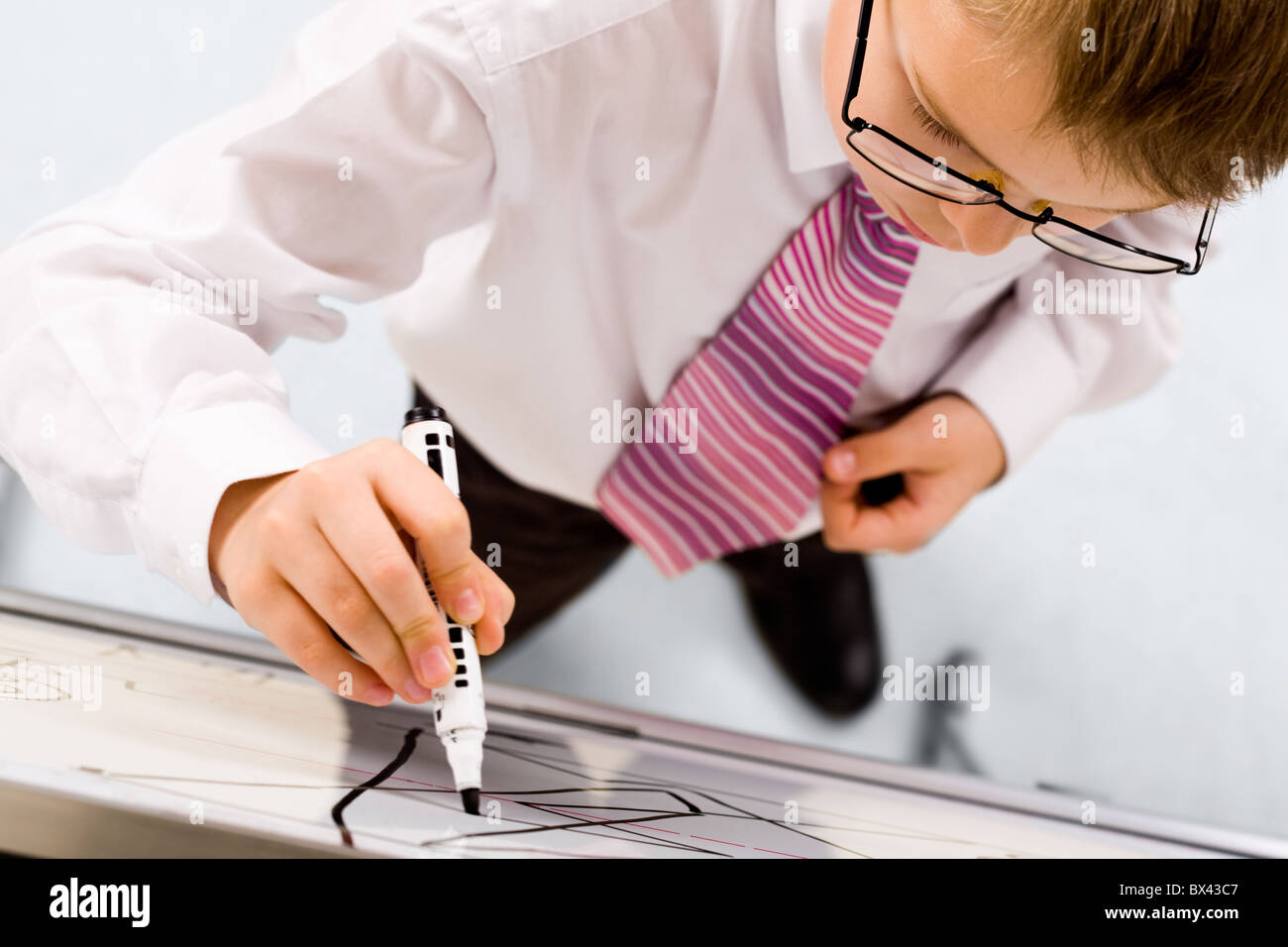 Smart boy with pen in hand standing by whiteboard and writing on it ...