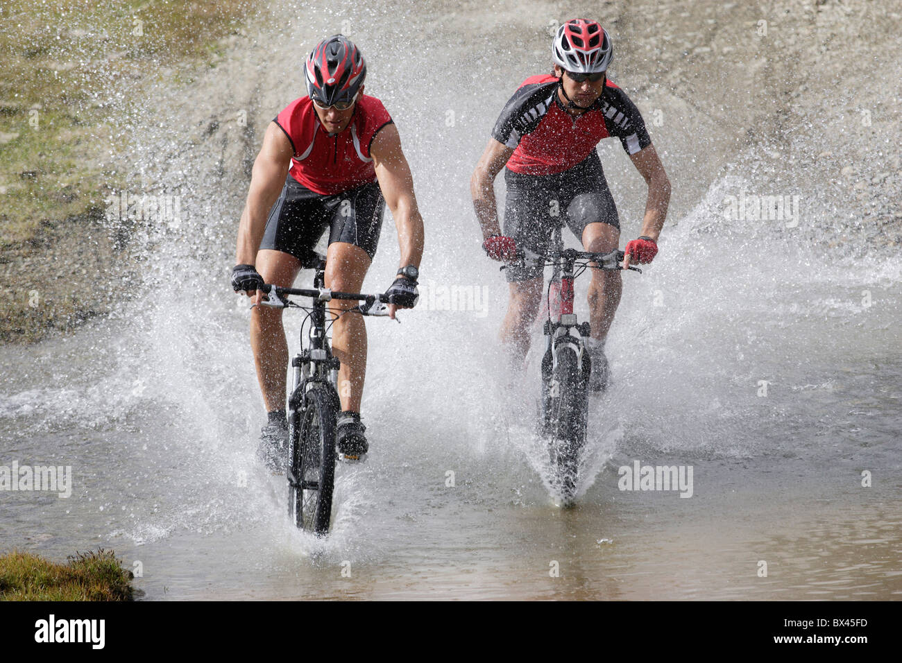 two persons men water brook stream splash Biking mountains Alps bicycle biking mountain bike bike sports Stock Photo