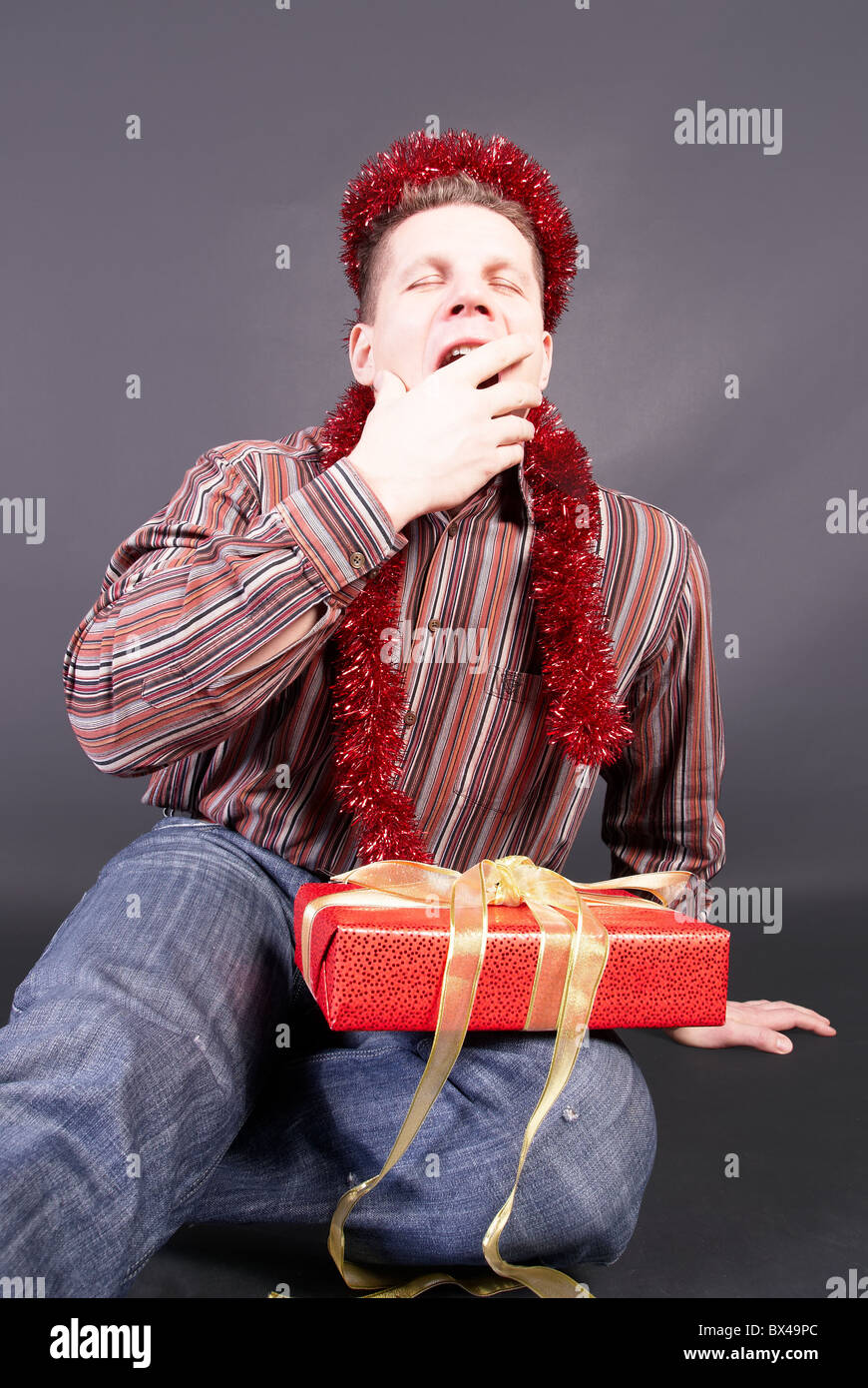 A man yawns, laying  the not opened gift on knees Stock Photo