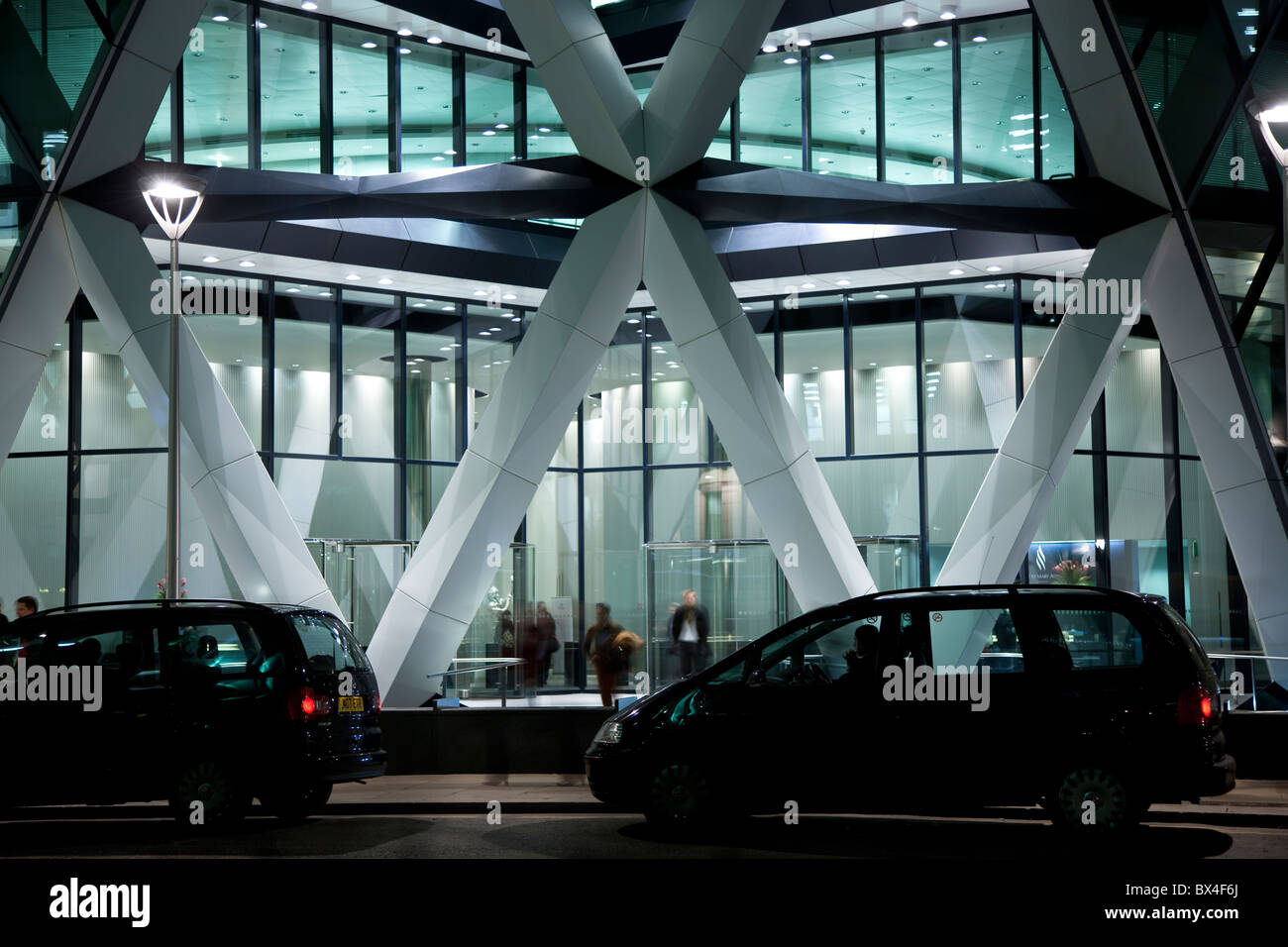 Cars parked in front of an illuminated futuristic office building at night, St Mary Axe, the Gherkin, the Swiss Re building Stock Photo
