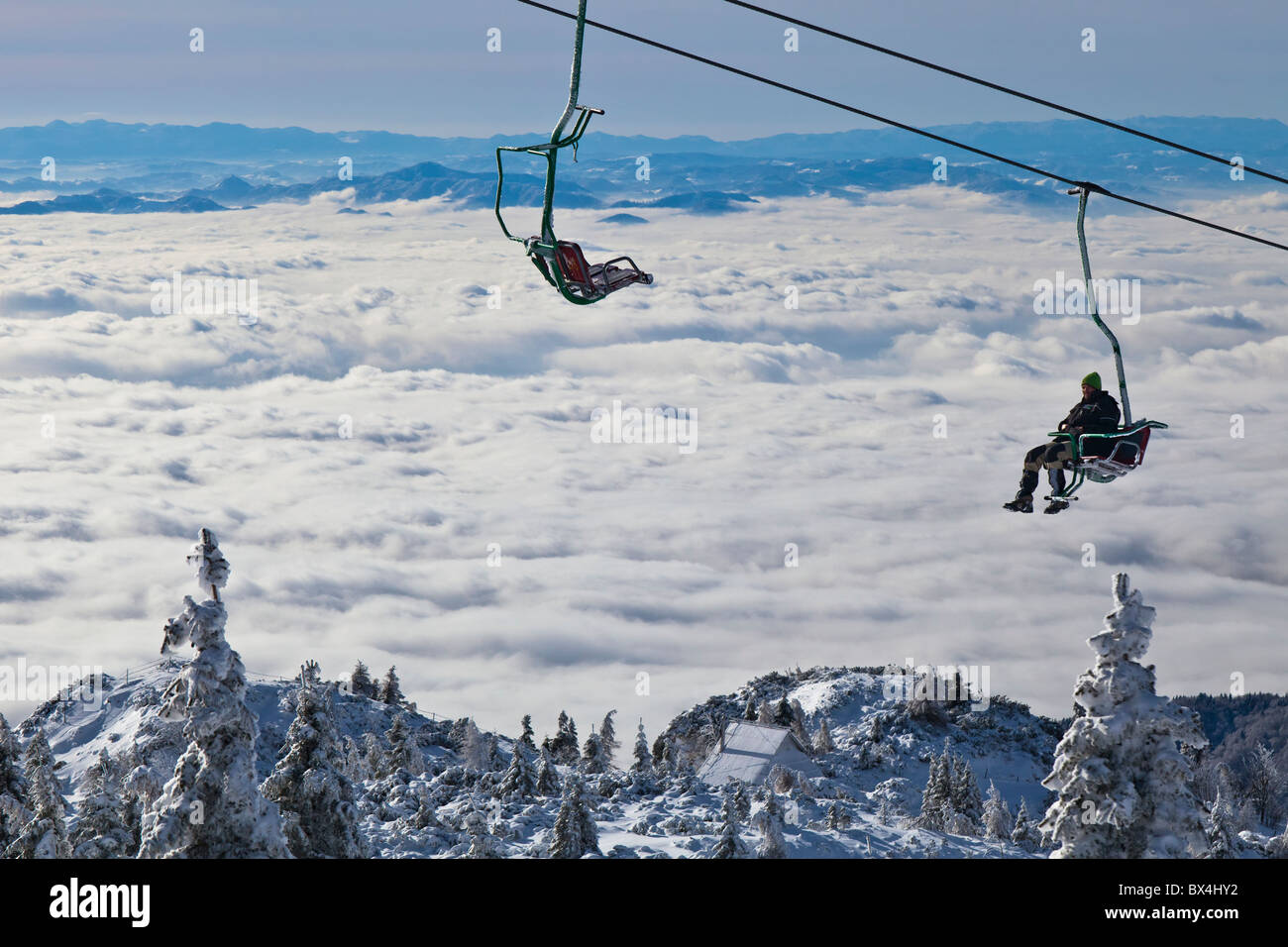 A man rides a chair lift over a sea of fog covering the Ljubljana basin. Velika Planina, Slovenia. Stock Photo