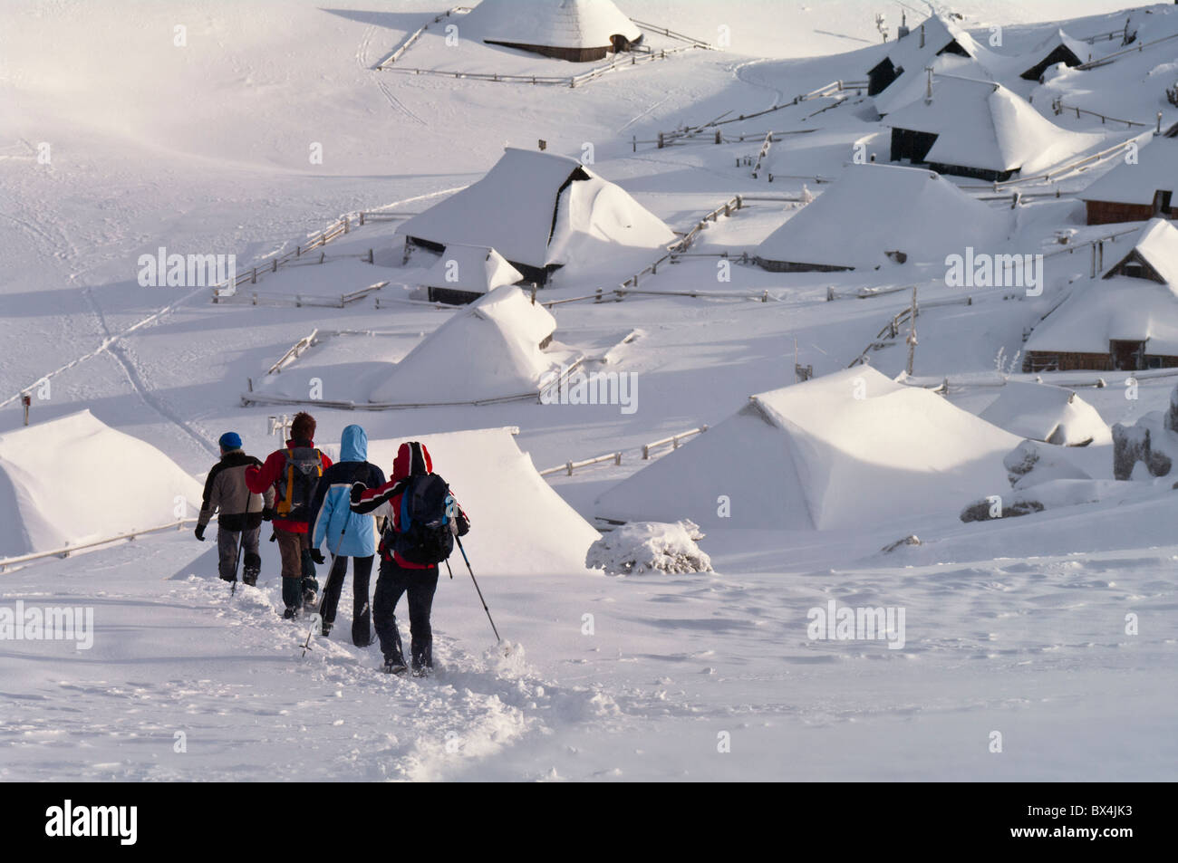 Trekkers descend a hill above shepherds' houses at Velika Planina, Slovenia. Stock Photo