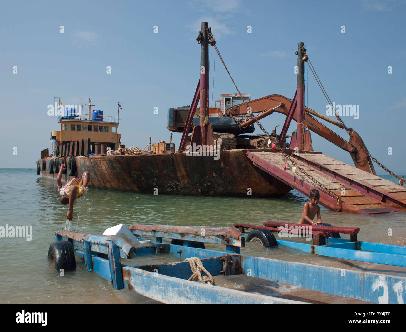 The boys are jumping swimming next to the rusty boat on the beach Stock Photo
