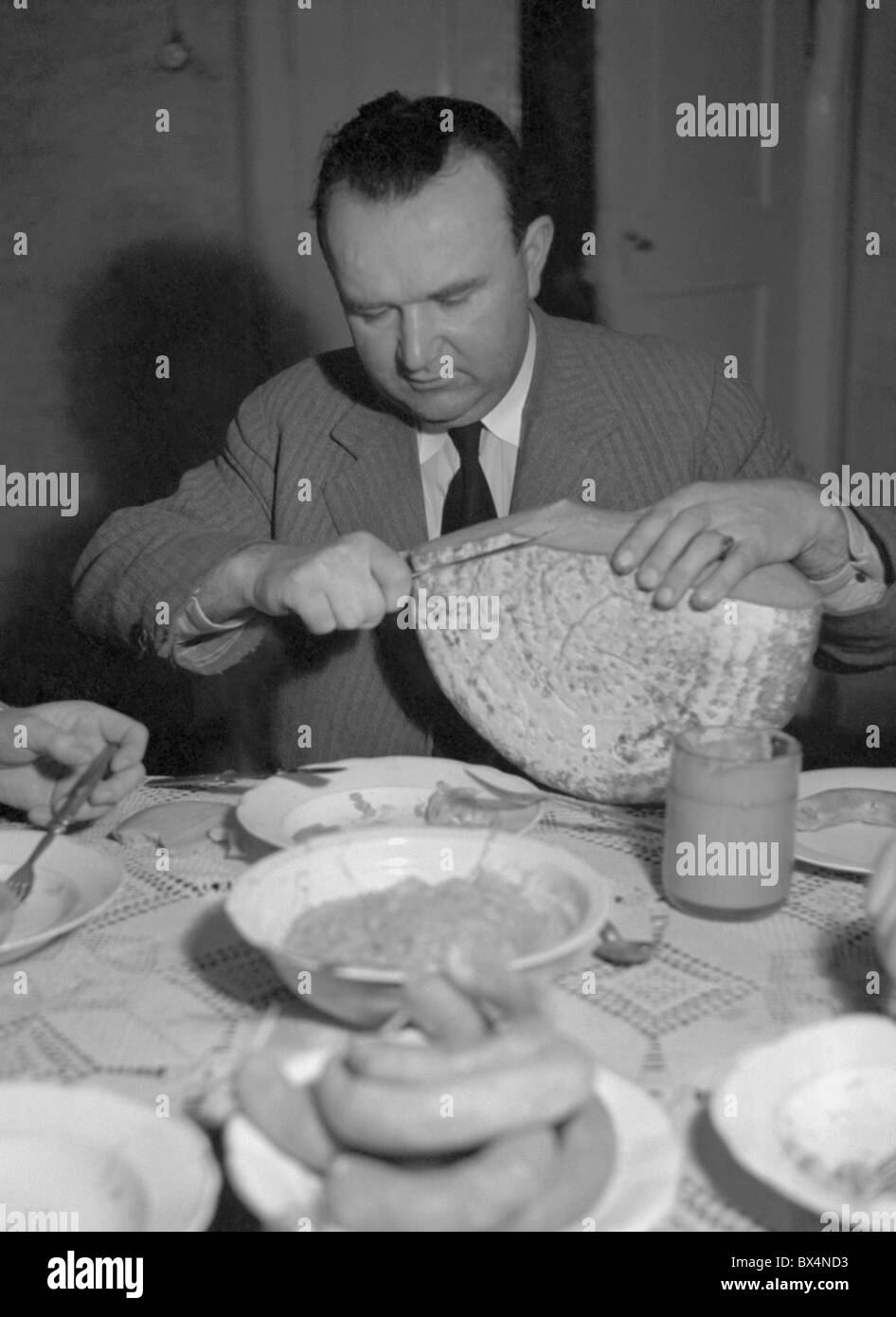 Czechoslovakia 1939, traditional home style hog slaying. Man slicing loaf of bread before feast Stock Photo