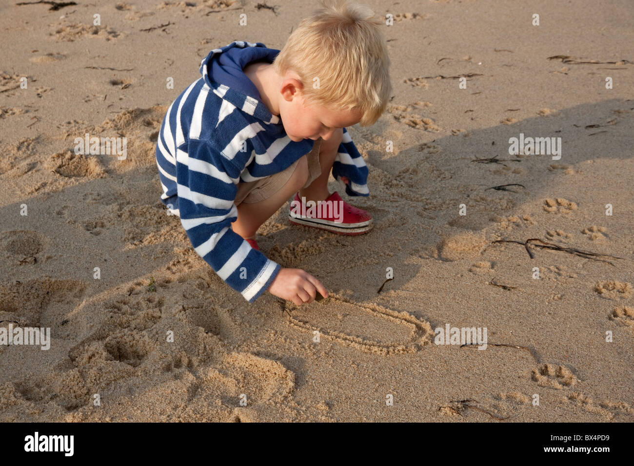 Child writing in the sand, practicing writing the number '0.' Stock Photo