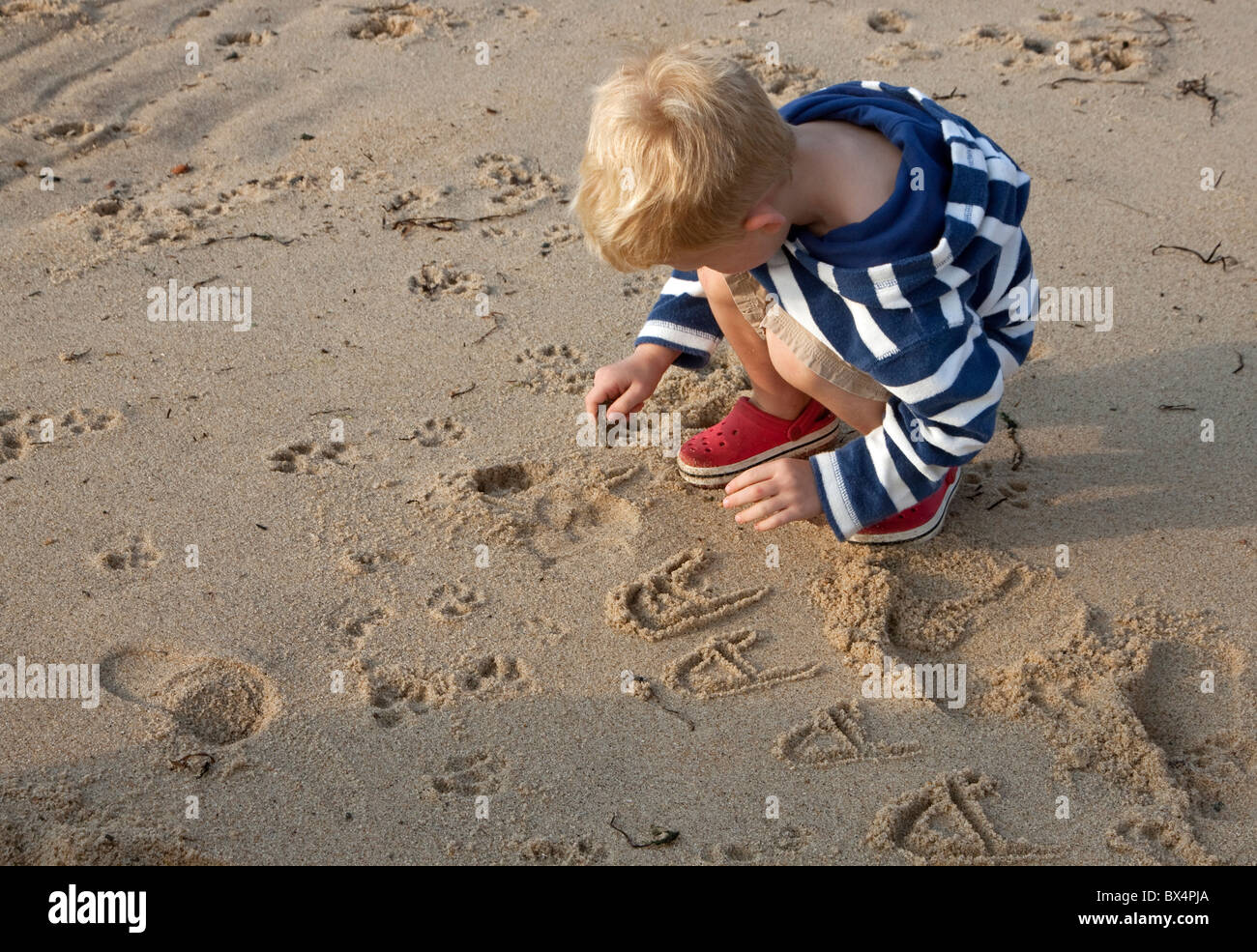 Child writing in the sand, practicing writing the letter 'A.' Stock Photo