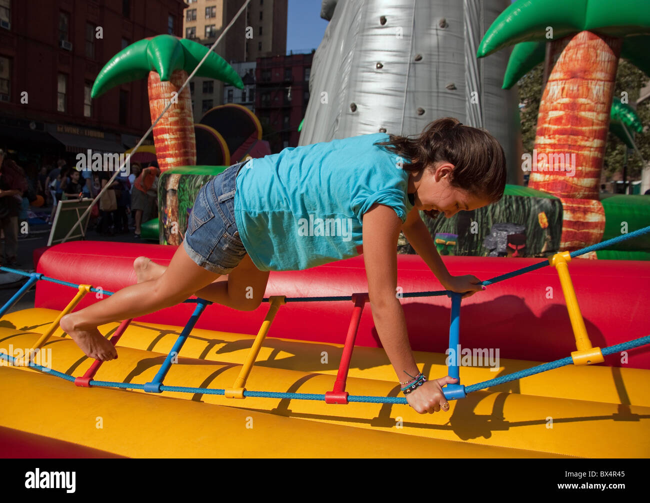 Young teen girl balancing on a rope ladder at a street fair, testing her skill and coordination. Stock Photo