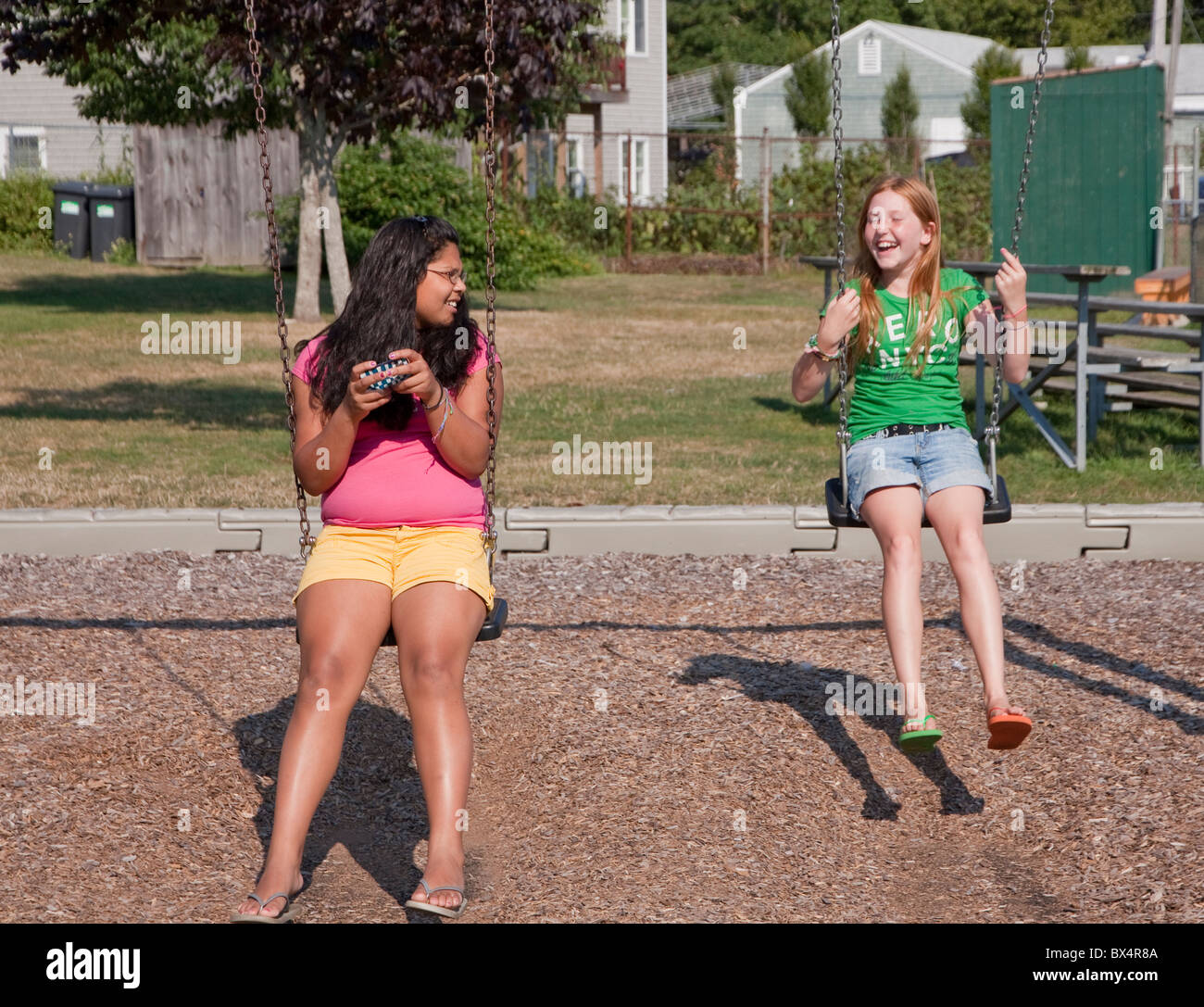 Two young teenage friends talking and laughing with each other in a playground. Stock Photo