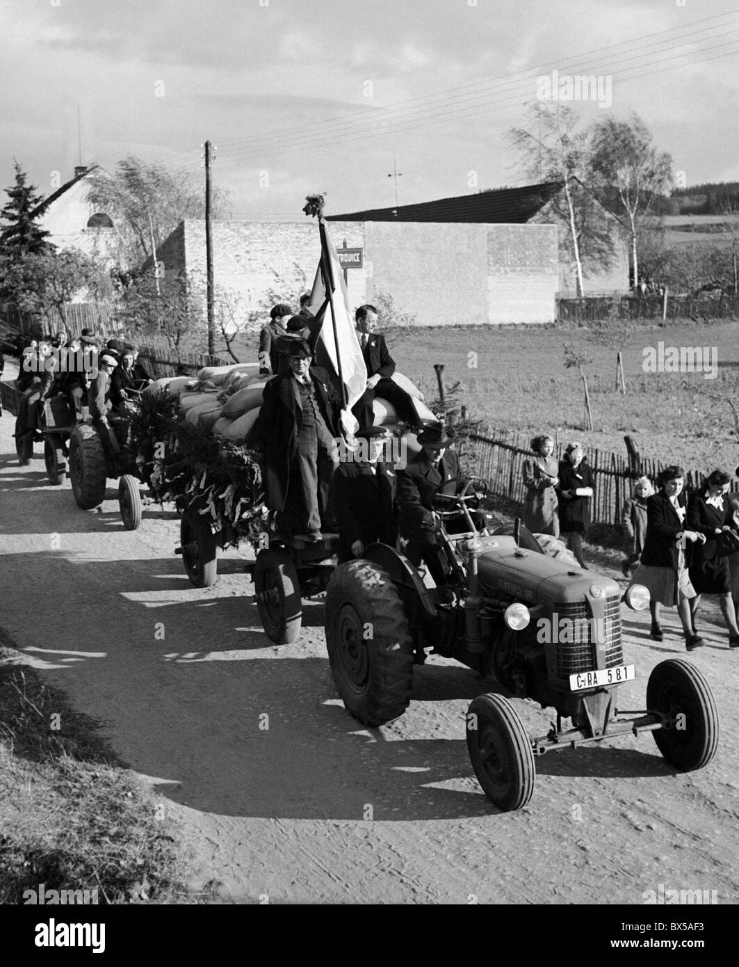 Czechoslovakia - Petrovice 1949. Cooperative farmers self celebrate a successful grain harvest. The tractor carries bags of Stock Photo