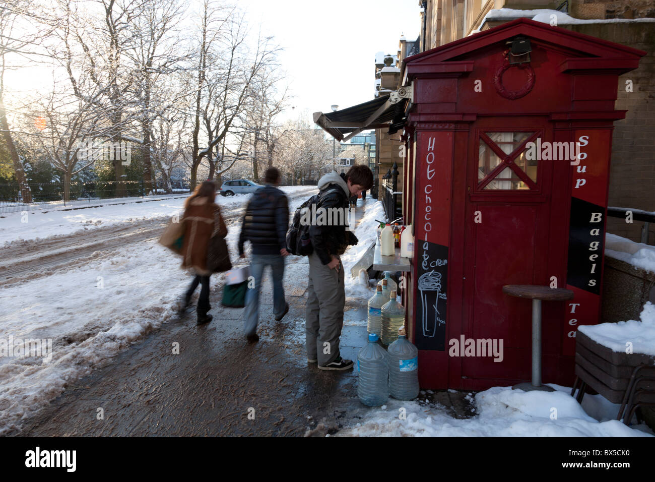 A male student buying a hot drink at a converted police box stall on a snowy Edinburgh street Stock Photo