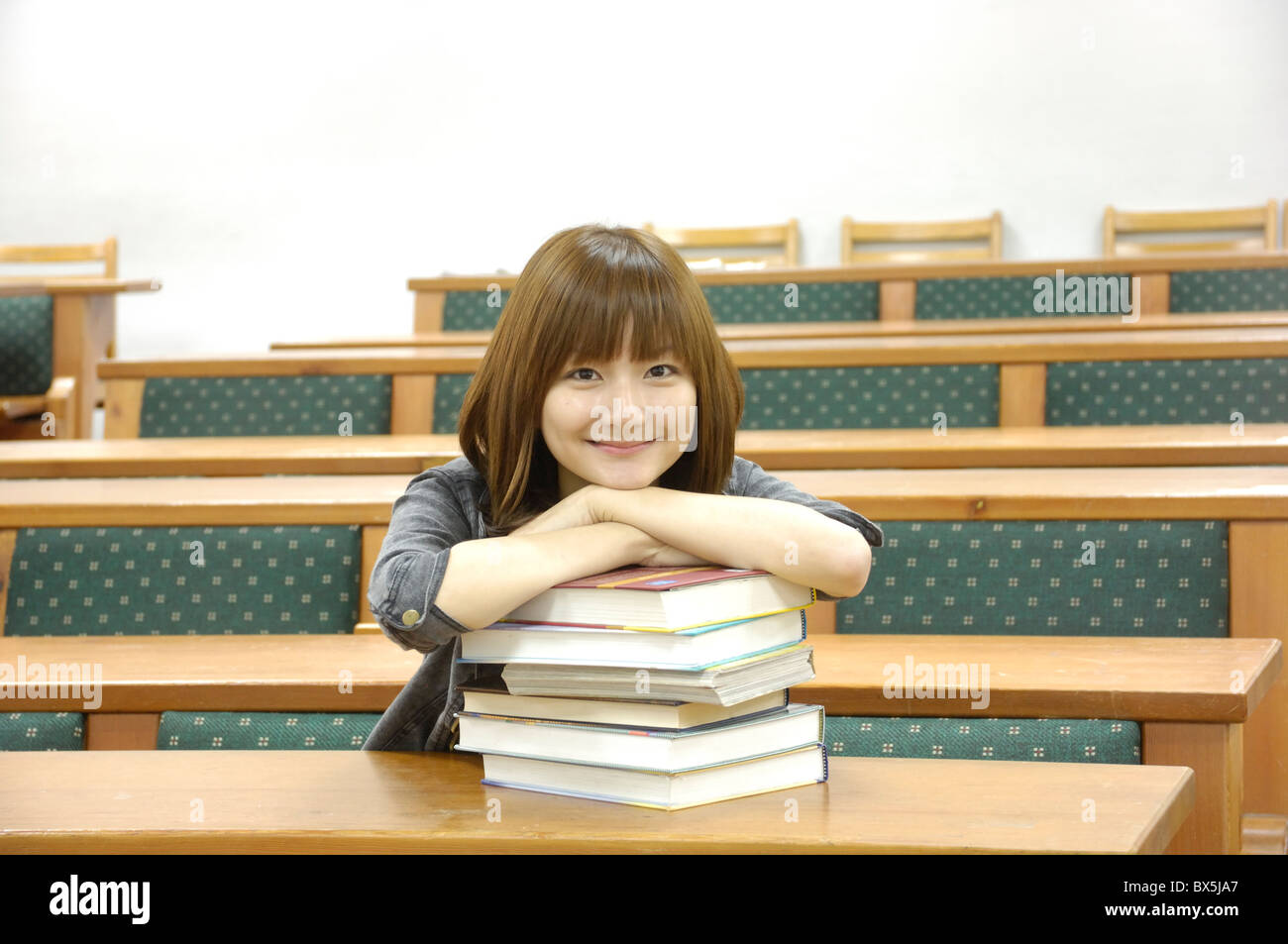 Female university student leaning on a stack of books in a classroom ...