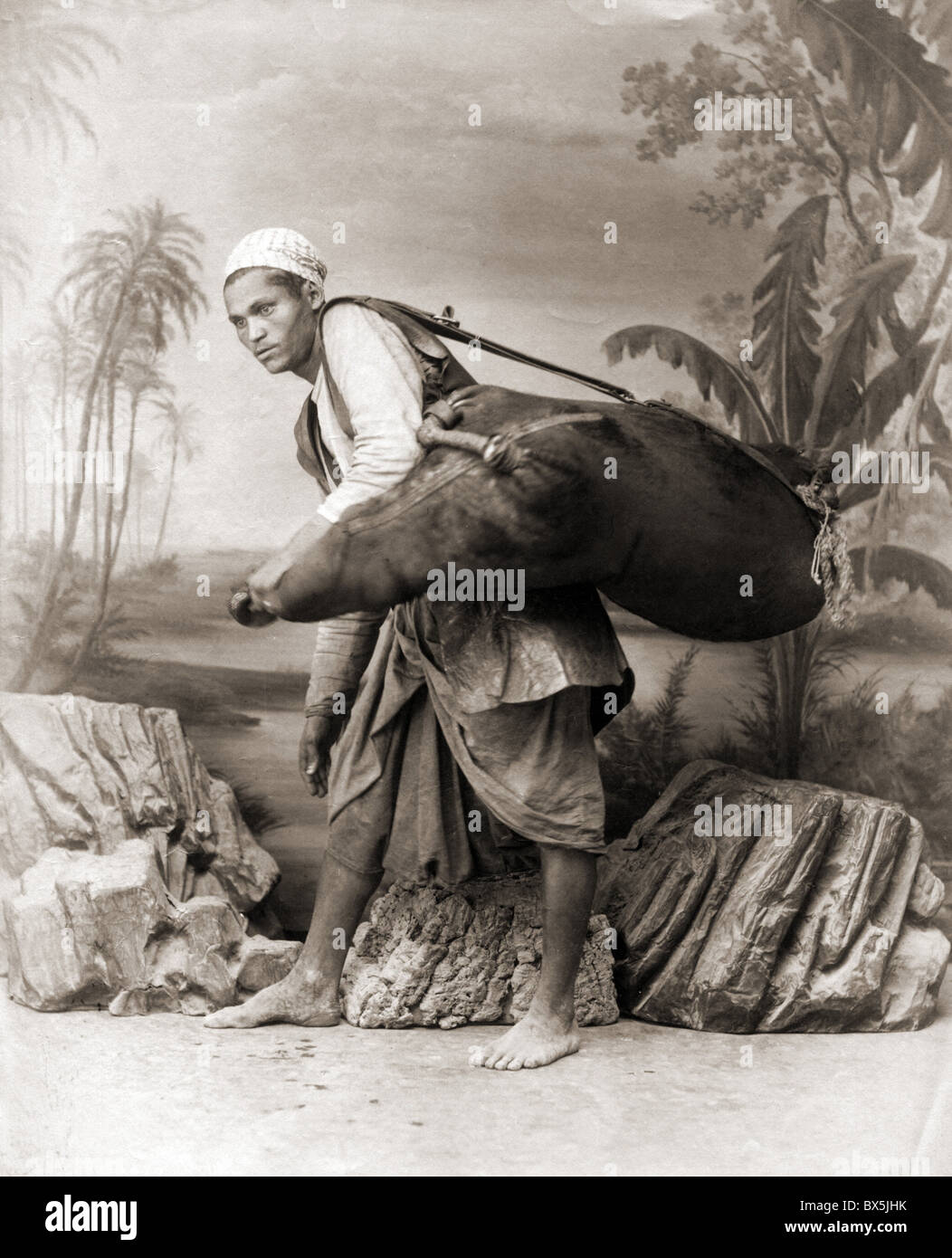 people, men, Africa, man carrying a bag, studio shot by J. P. Sebah, late 19th century, water, oasis, oases, ethnicities, ethnic, ethnology, North African, rocks, historic, historical, carrier, male, Additional-Rights-Clearences-Not Available Stock Photo