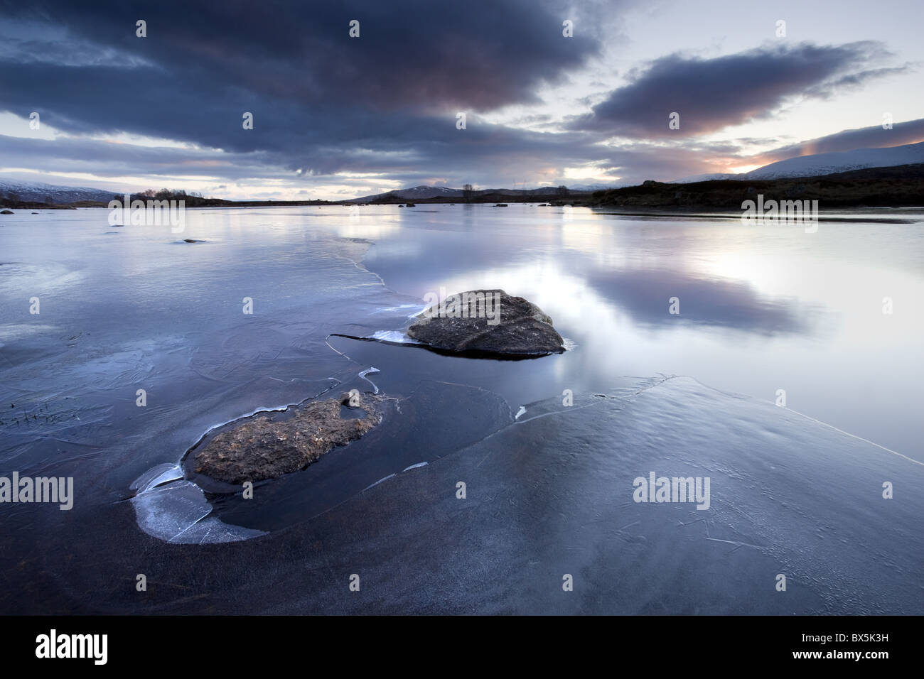 Winter view of Loch Ba' at dawn, loch partly frozen with two large rocks protruding from the iceg, Rannoch Moo, Scotland, UK Stock Photo