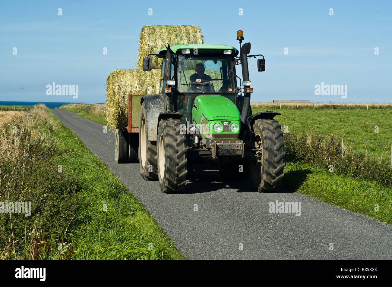 dh  FARMING ORKNEY Deutz Fahr tractor hauling trailer carrying cyclinder bales road uk farm machine driver Stock Photo
