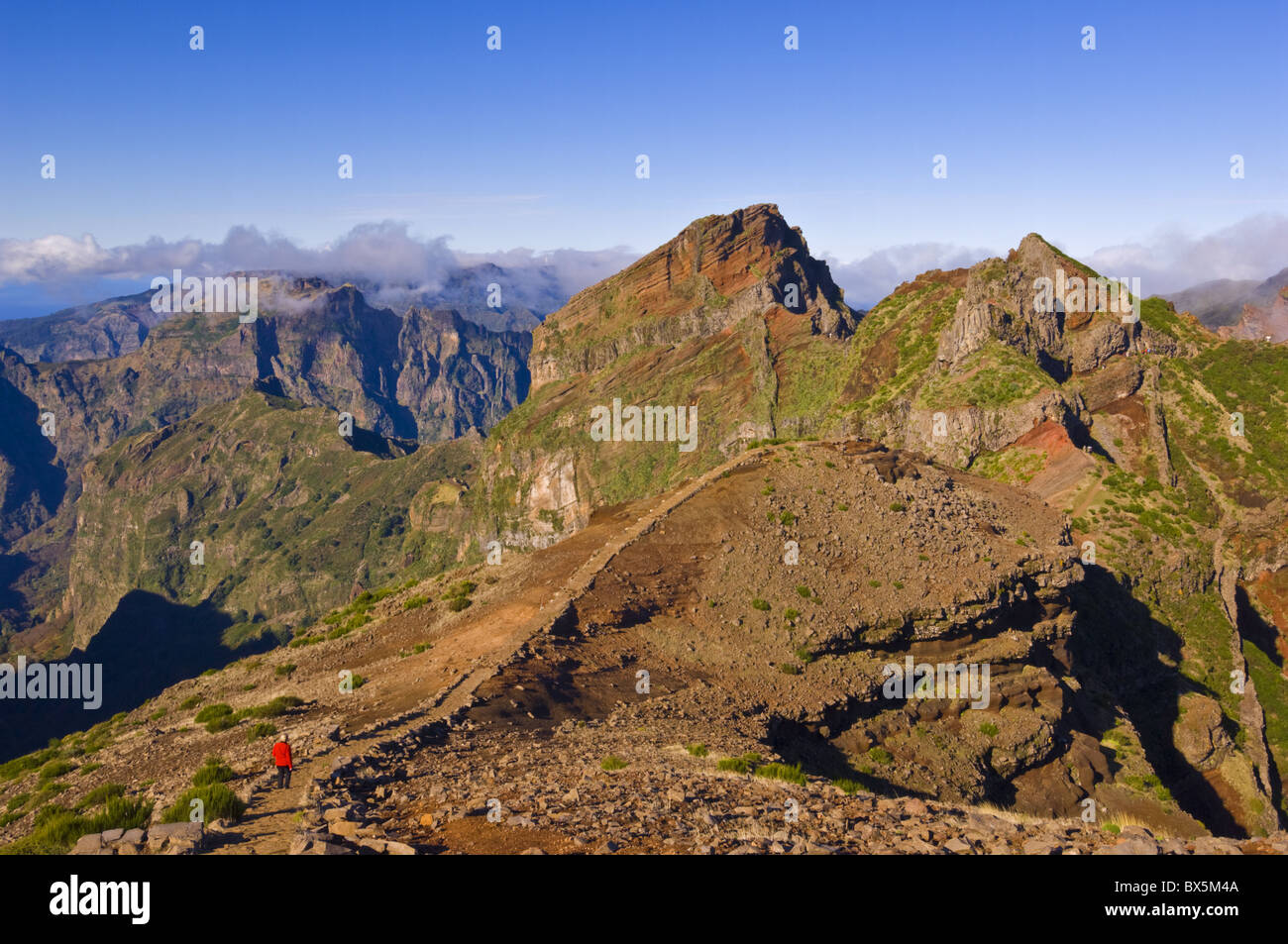 Hiker in red jacket walking down new footpath across the volcanic landscape towards Pico do Arieiro, Madeira, Portugal Stock Photo