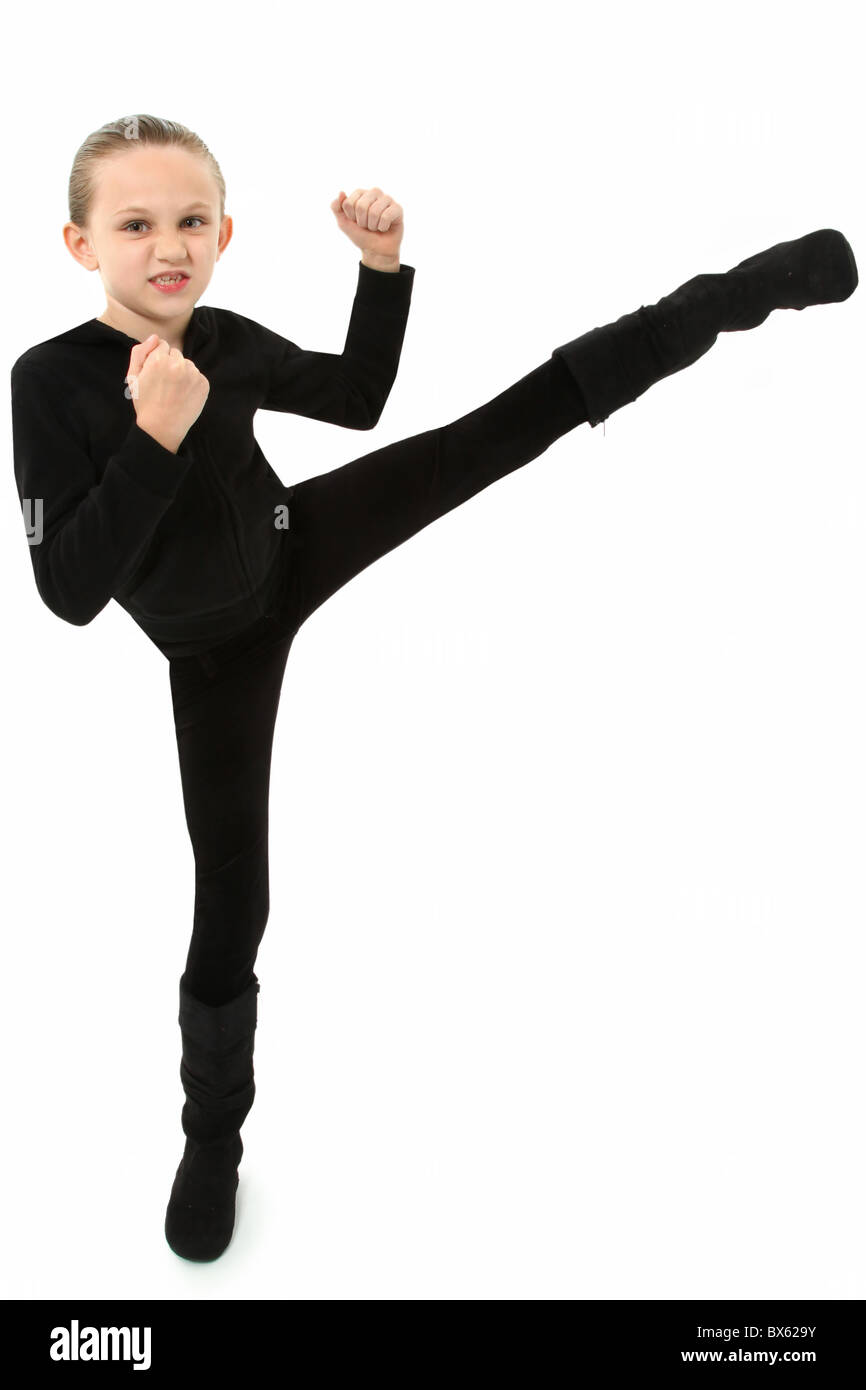Adorable 7 year old girl in black demonstrating a martial arts kick over white background. Stock Photo