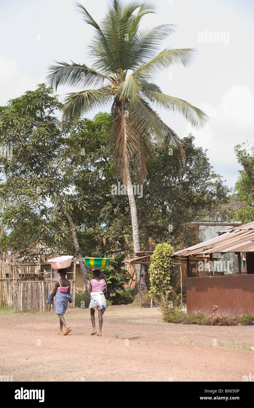 Girls with buckets balanced on their heads walk along the main street in Kakata, Liberia, West Africa. Stock Photo