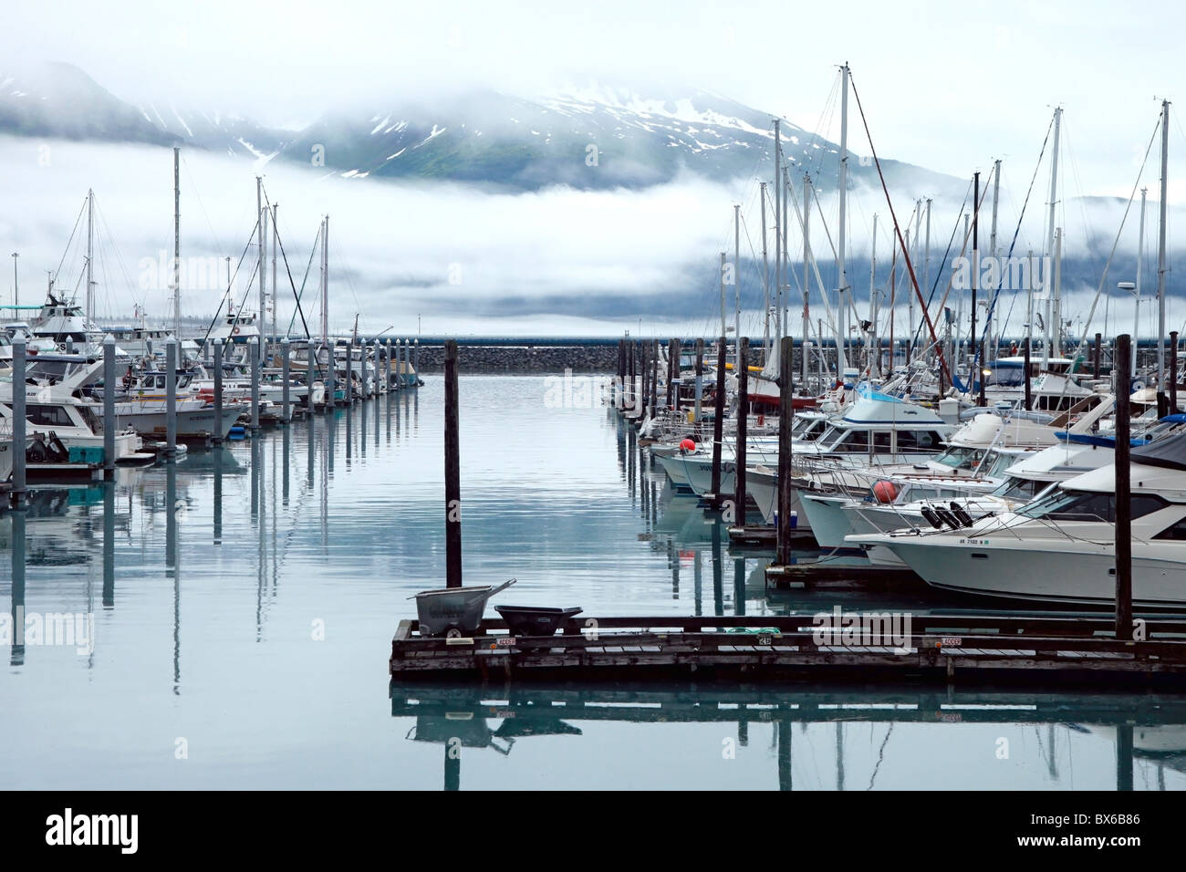 Boats on the ocean at a marina in bay with snowy mountains and low clouds in the distance at Valdez, Alaska, USA. Stock Photo