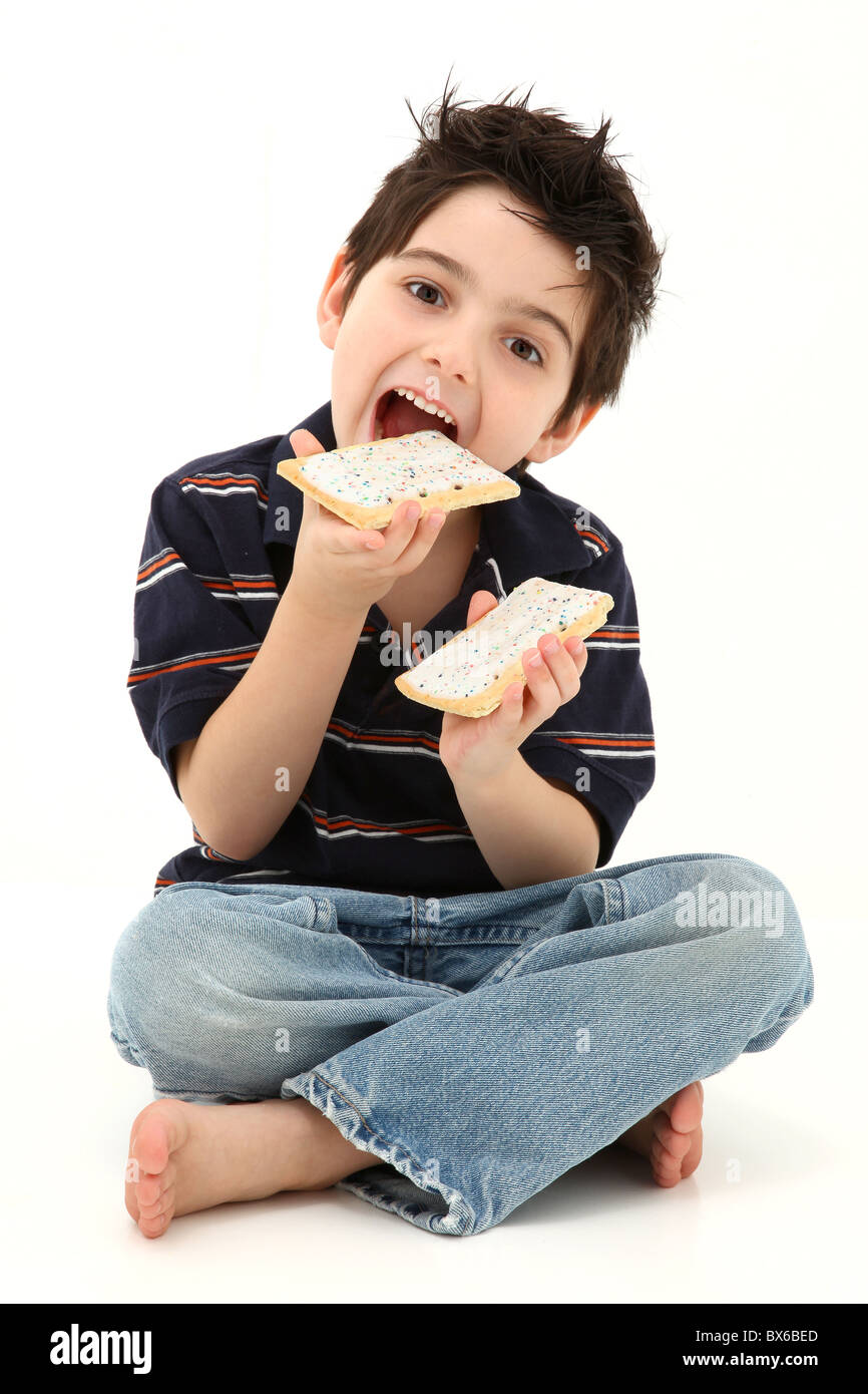 Adorable six year old boy laughing and eating pop tarts. Sitting on white floor. Stock Photo