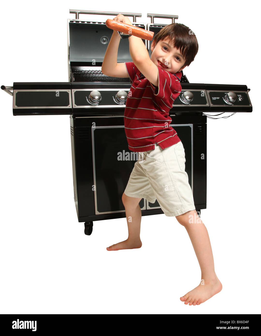 Adorable seven year old boy with grill utensils in front of large gas grill. Stock Photo