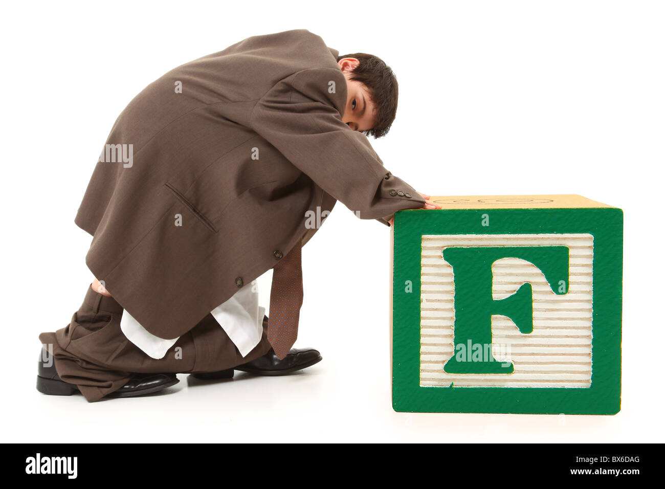 Adorable boy in large suit pushing giant letter F alphabet block. Stock Photo