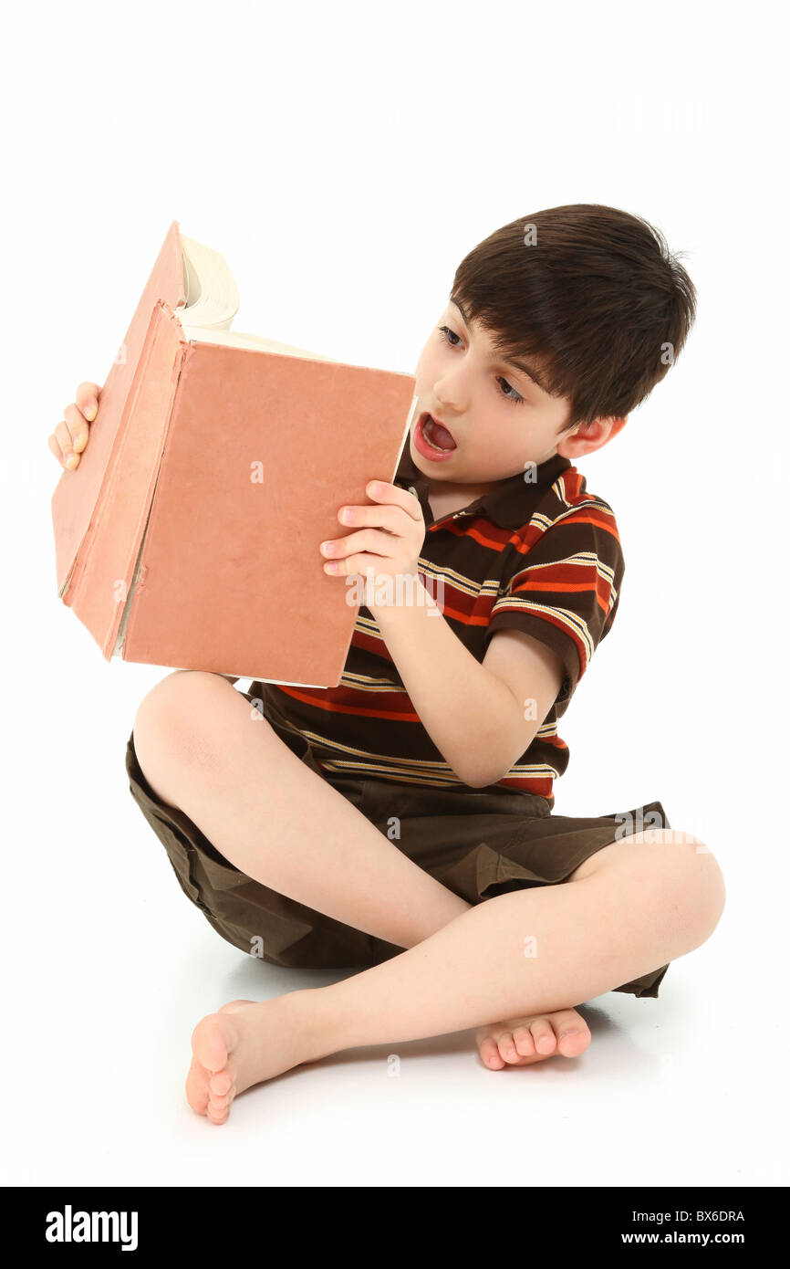 Adorable seven year old french american boy reading large book over white background. Stock Photo