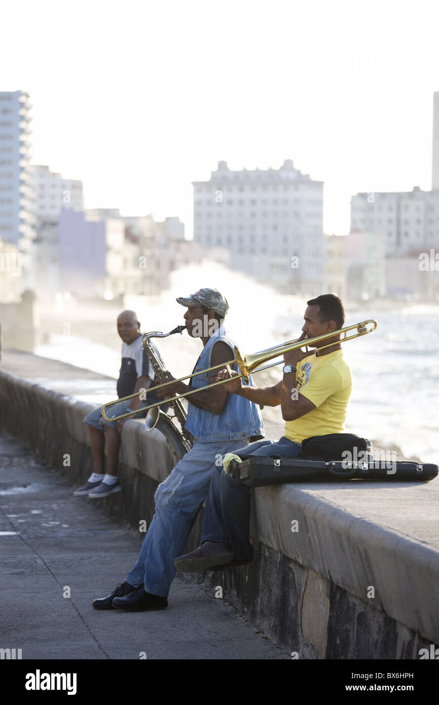 Musicians on The Malecon playing saxaphone and trombone with waves crashing against the shore in the background, Havana, Cuba Stock Photo