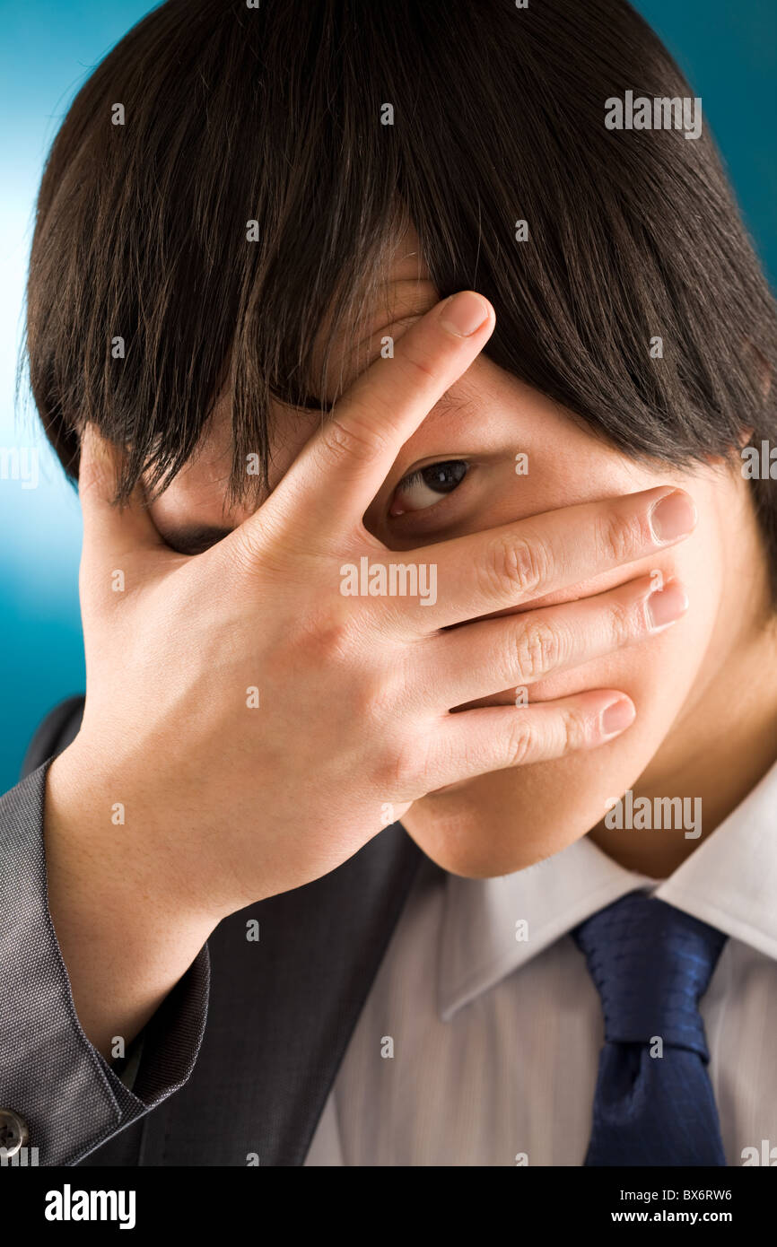 Portrait of young businessman looking at camera from behind his hand Stock Photo