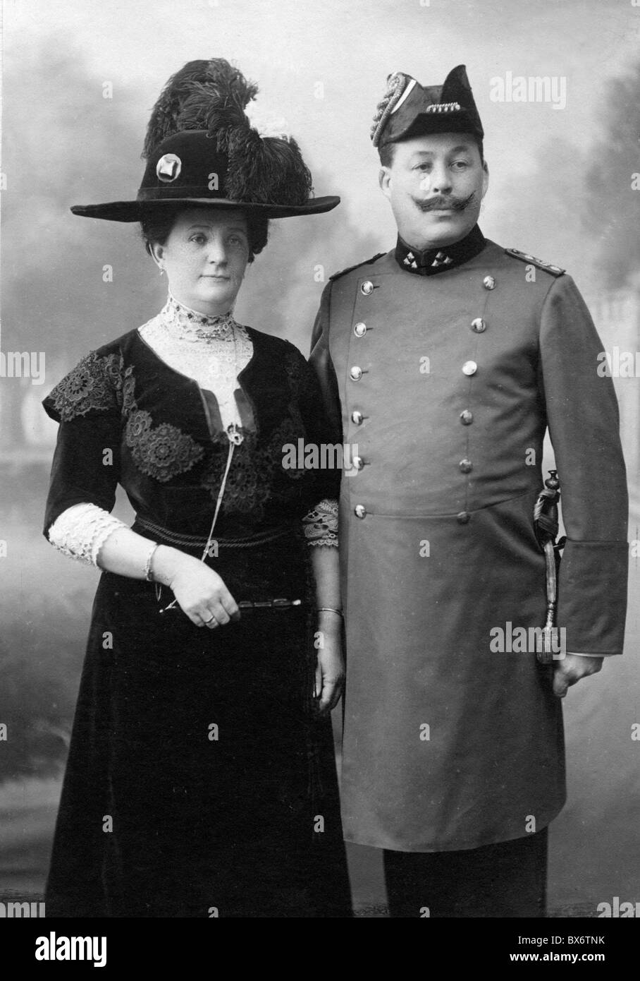 people, couples, 1900 - 1930, smartly dressed couple with man in uniform of a civil servant, circa 1900, Germany, German Empire, half length, standing, clothes, outfit, outfits, fashion, hat, hats, feather, feathers, bicorn, moustache, mustache, moustaches, mustaches, uniform, uniforms, civil servant, civil servants, at the turn of the 19th / 20th century, festive, feastful, festal, couple, couples, historic, historical, woman, women, female, man, men, male, people, 1900s, Additional-Rights-Clearences-Not Available Stock Photo