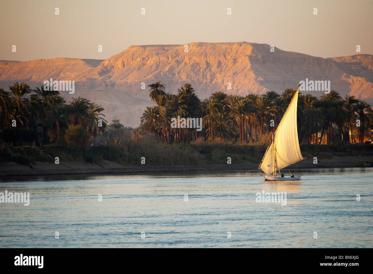 A stunning and beautiful image of a traditional Egyptian sail boat called a felucca on the Nile at sunset with mountains behind Stock Photo