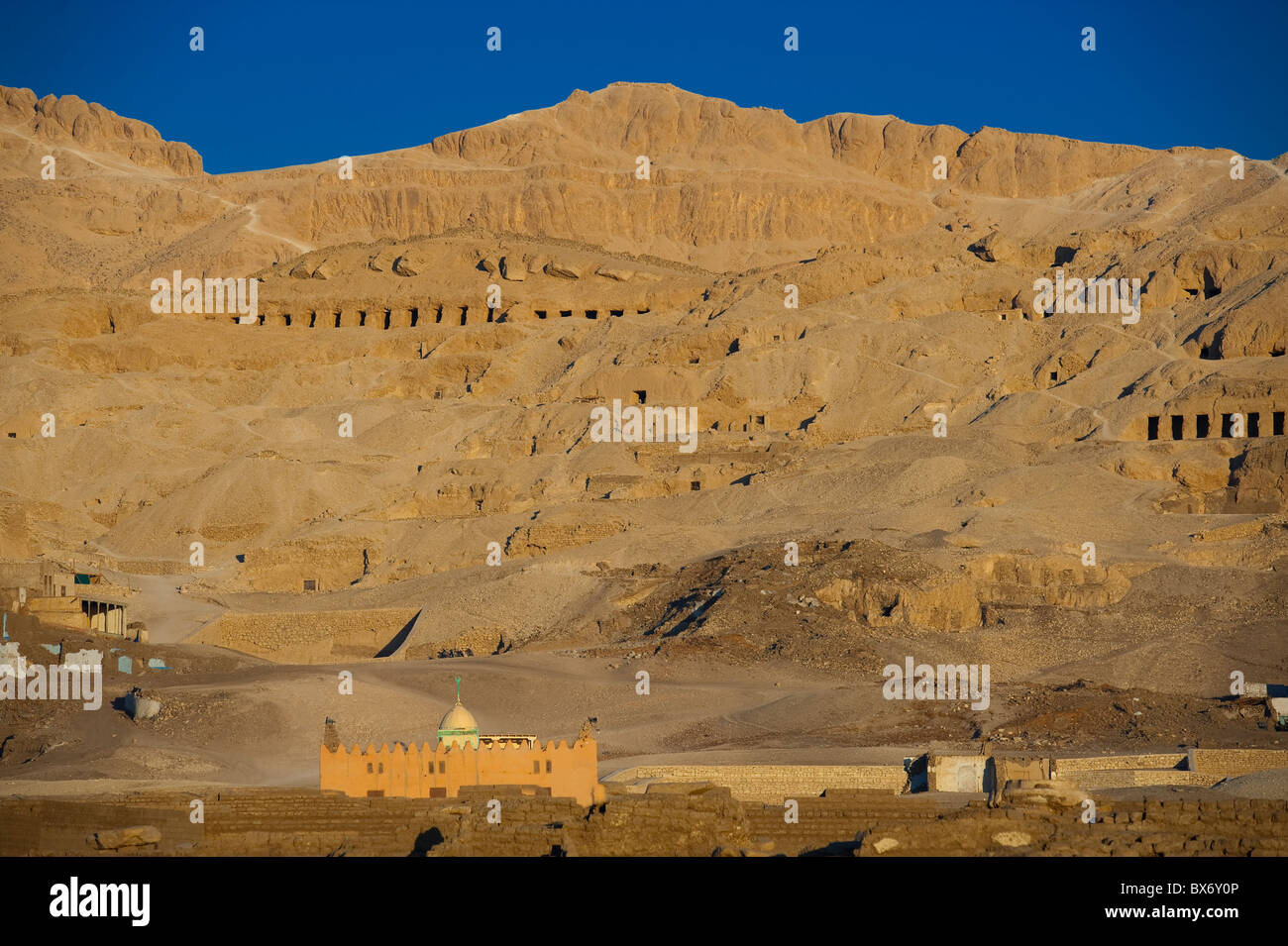 A long telephoto image of the Valley of the Kings in Egypt at sunrise with a mosque in the foreground Stock Photo